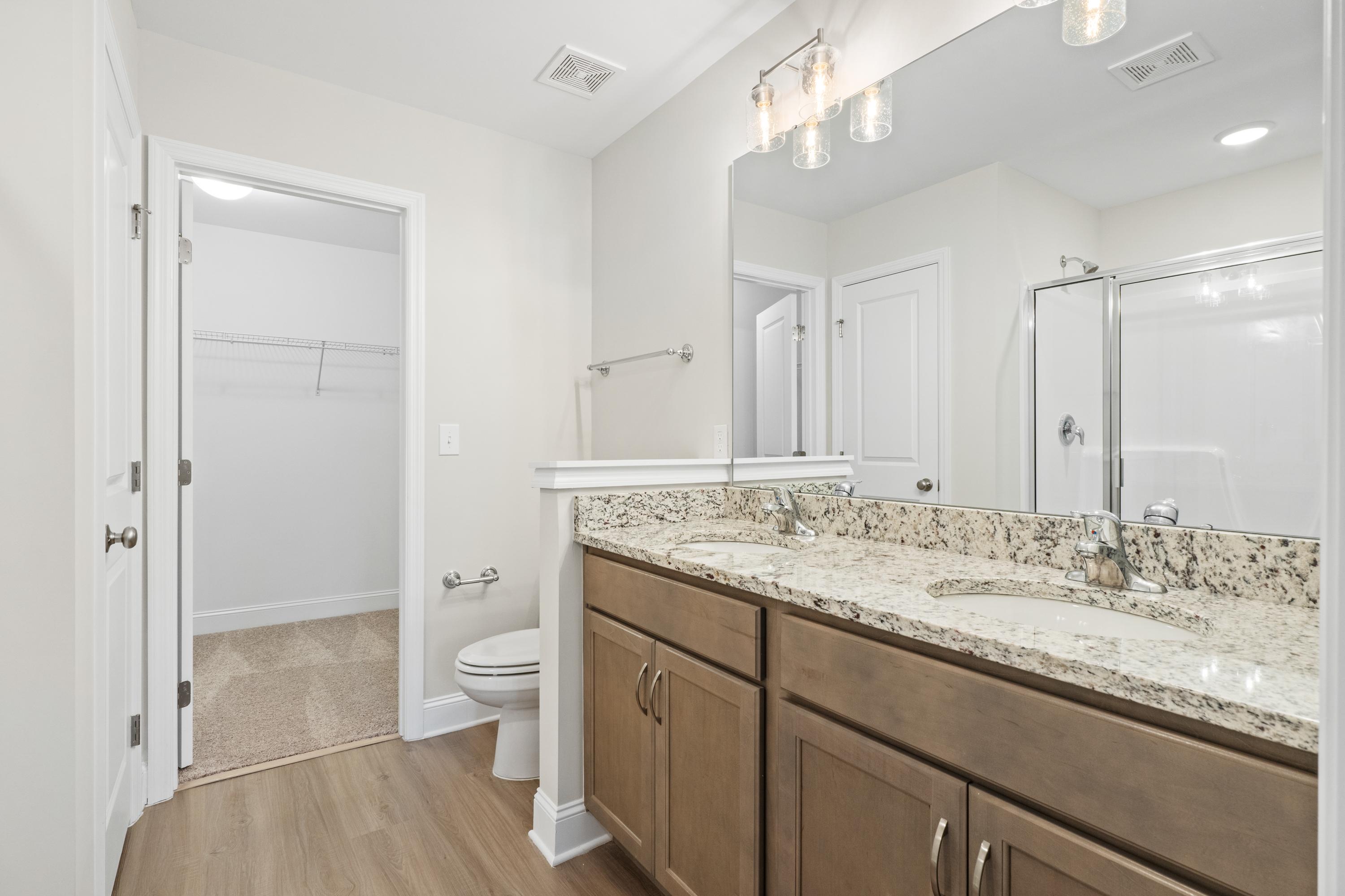 Spacious master bathroom in The Asheville with double granite vanity, wood cabinets, glass shower, and neutral tones