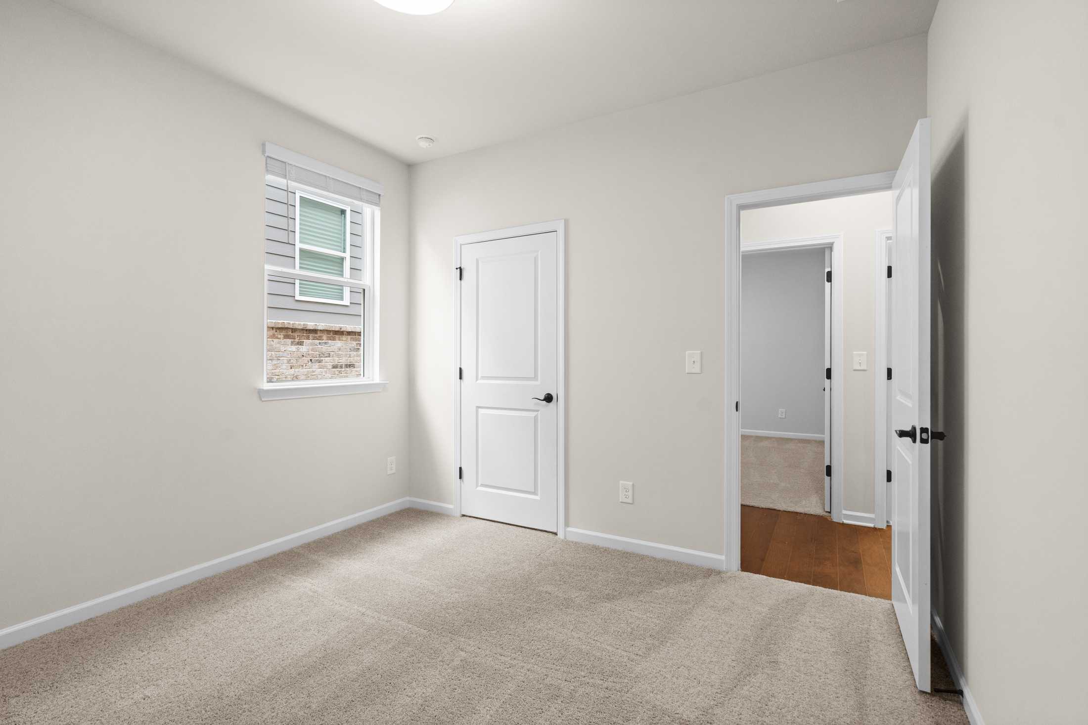 Spacious secondary bedroom in The Glenwood B featuring beige carpet, neutral walls, white doors, and wood-floor hallway