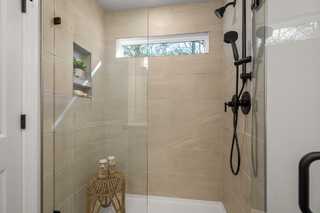 Spacious walk-in shower in The Washington H master bath with frameless glass doors, beige tiles, rain showerhead, and niche shelves