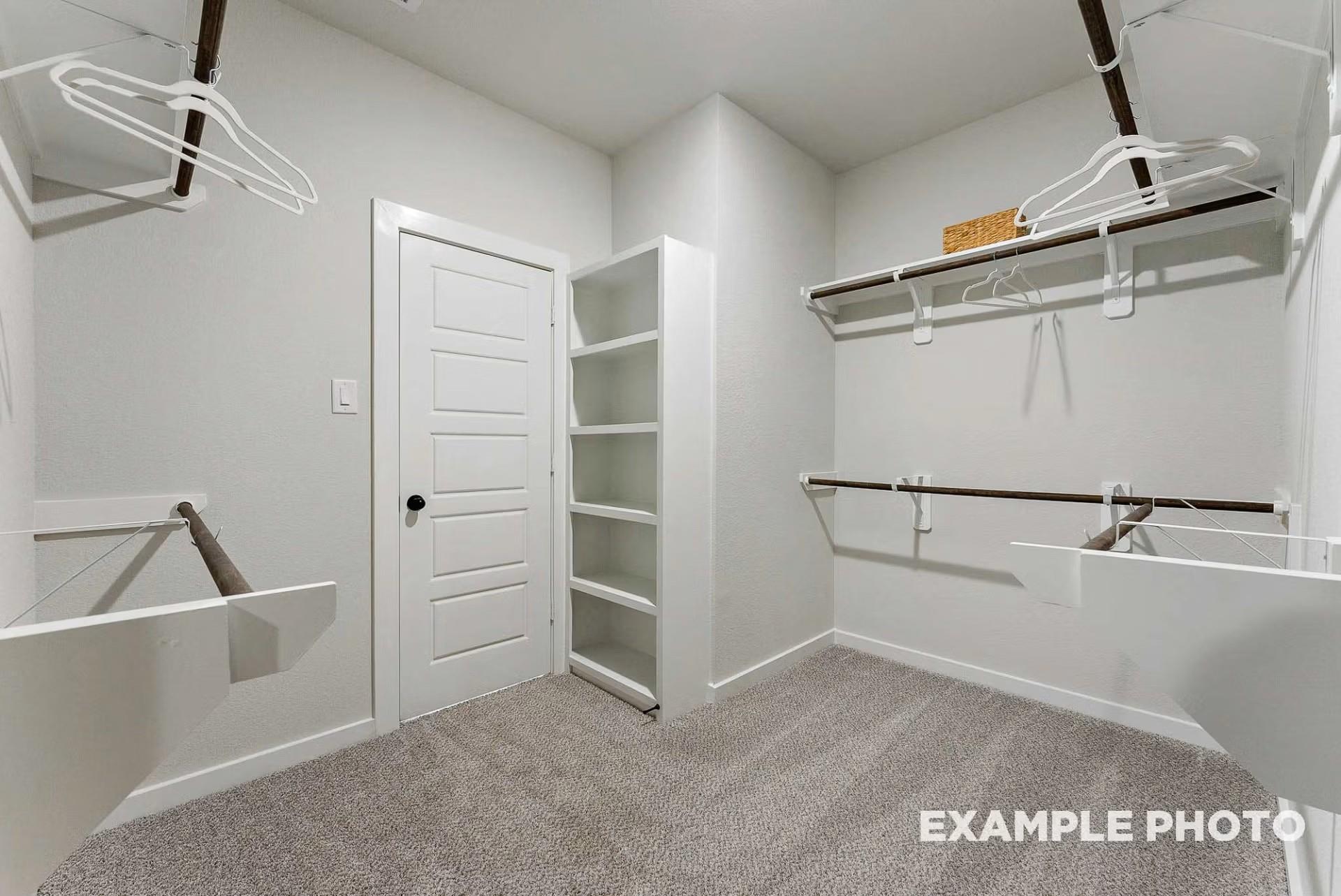 Spacious walk-in closet with wooden rods, open shelves, white hangers, and gray carpet in Davidson Homes The Everett C, Dayton, Texas