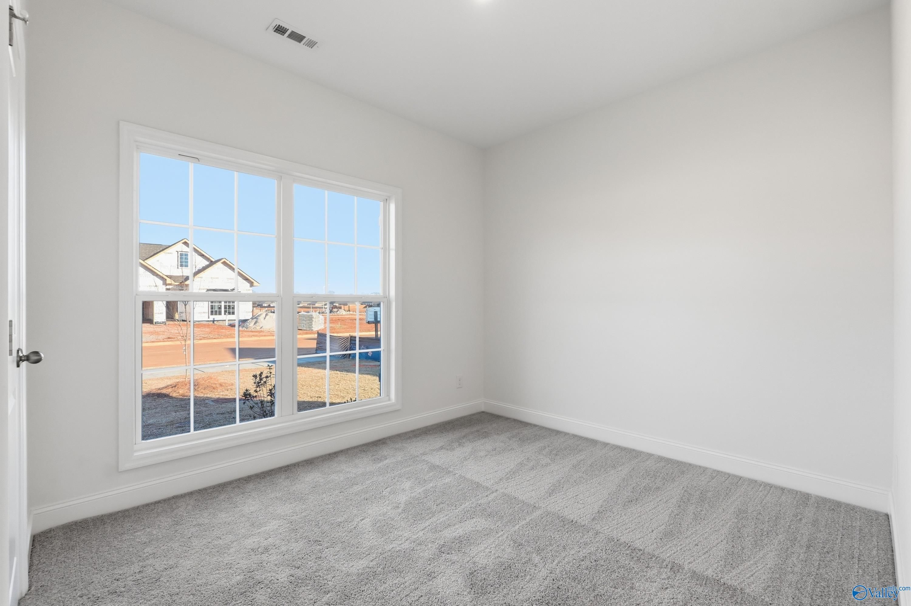 Bright empty bedroom with large window overlooking new homes, gray carpet, white walls in Asheville C by Davidson Homes, Meridianville AL