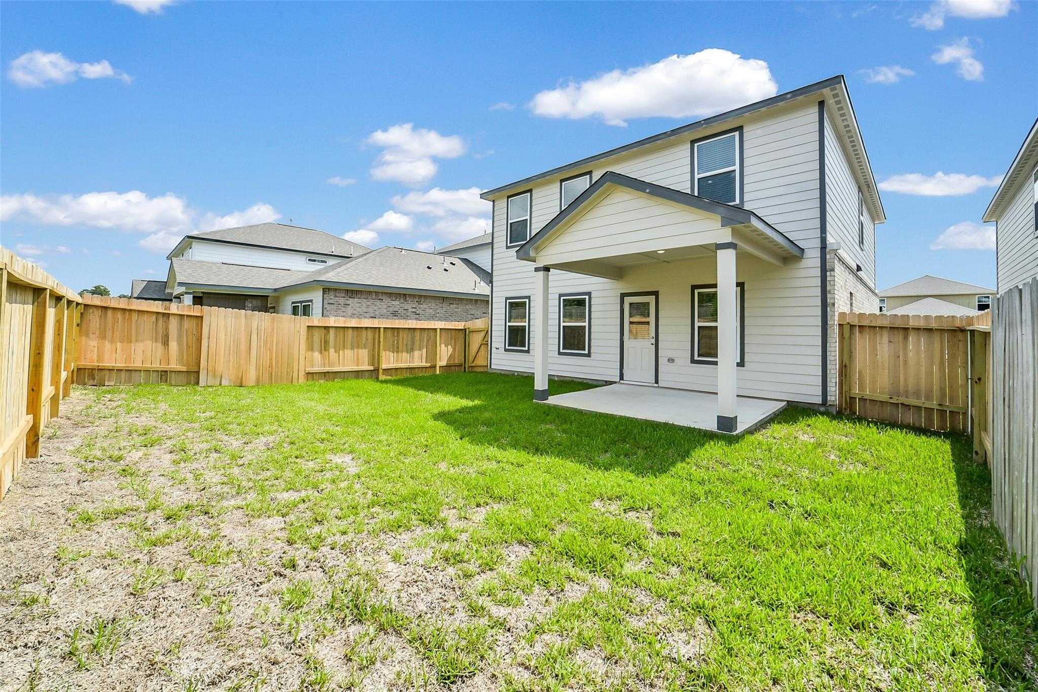 Rear view of The Trinity F two-story home with covered patio and spacious fenced backyard in Lakes at Black Oak, Magnolia, Texas