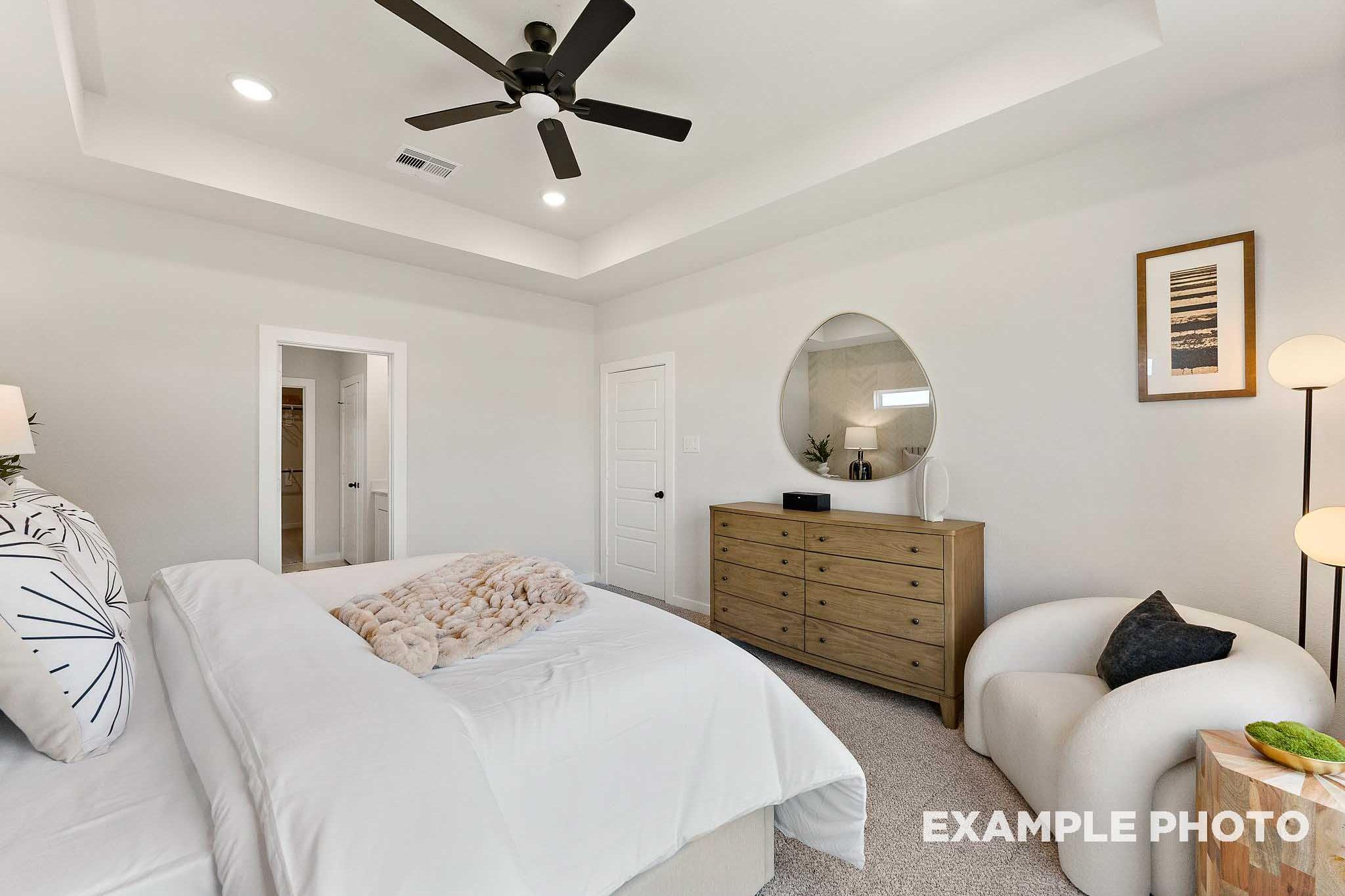 Serene master bedroom in The Everett E featuring king bed with pink throw, wooden dresser, round mirror, ceiling fan, and armchair