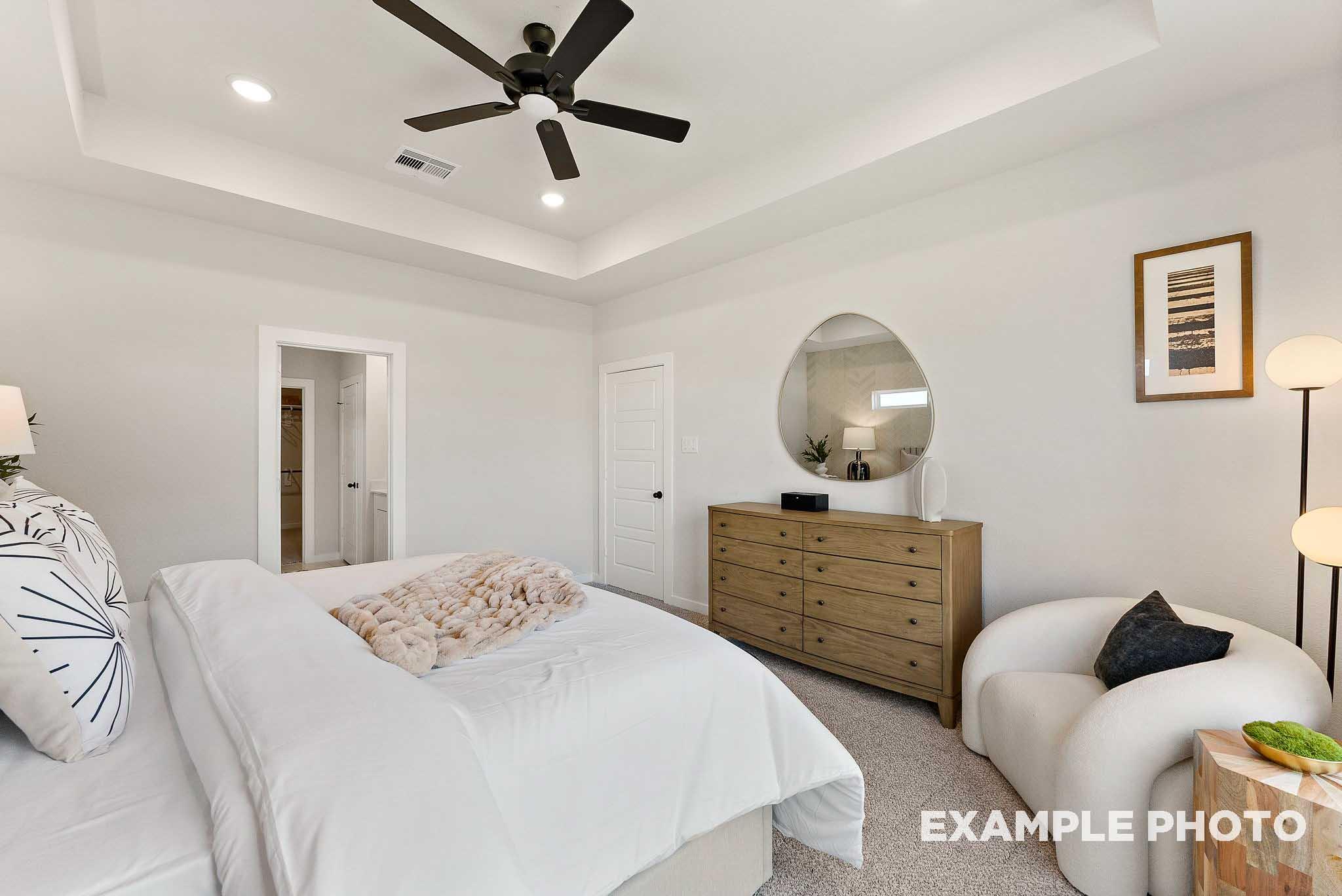 Bright primary bedroom with tray ceiling and modern decor in The Everett E floor plan by Davidson Homes in Crosby, TX.