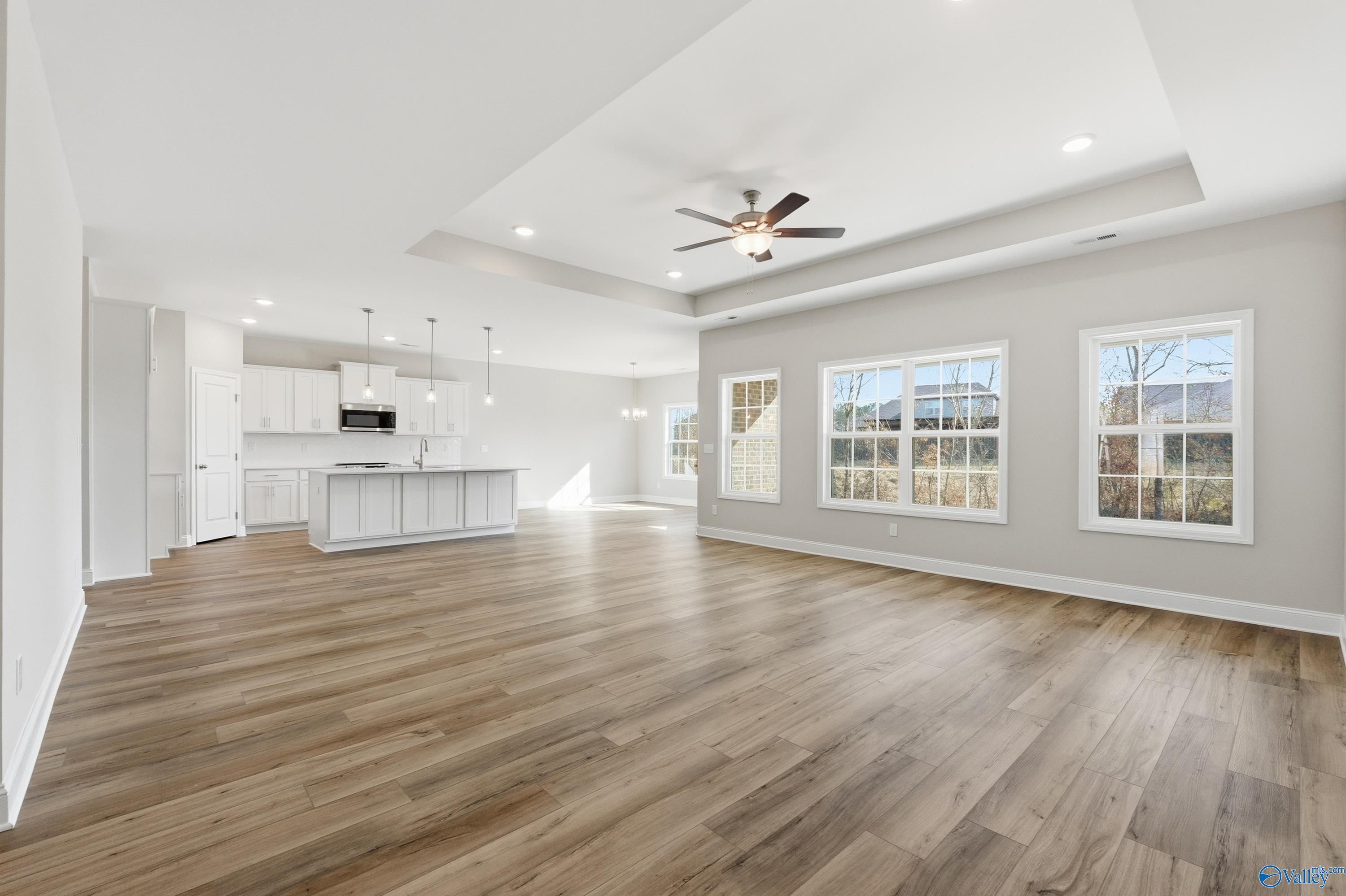 Open-concept kitchen and living area with white island, hardwood floors, ceiling fan, and large windows in Davidson Homes The Rockford, Harvest, AL