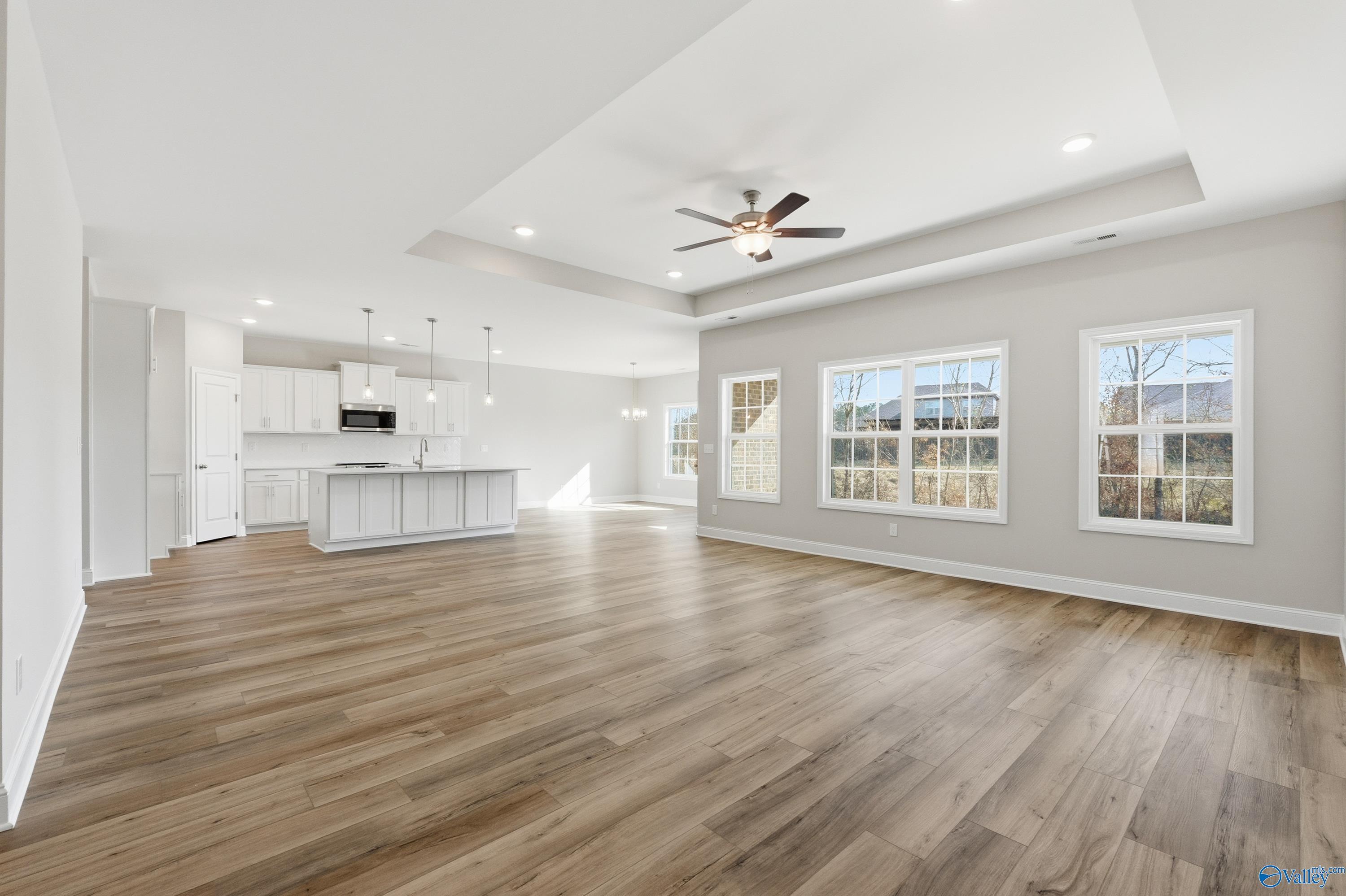 Open-concept kitchen and living area with white island, hardwood floors, ceiling fan, and large windows in Davidson Homes The Rockford, Harvest, AL