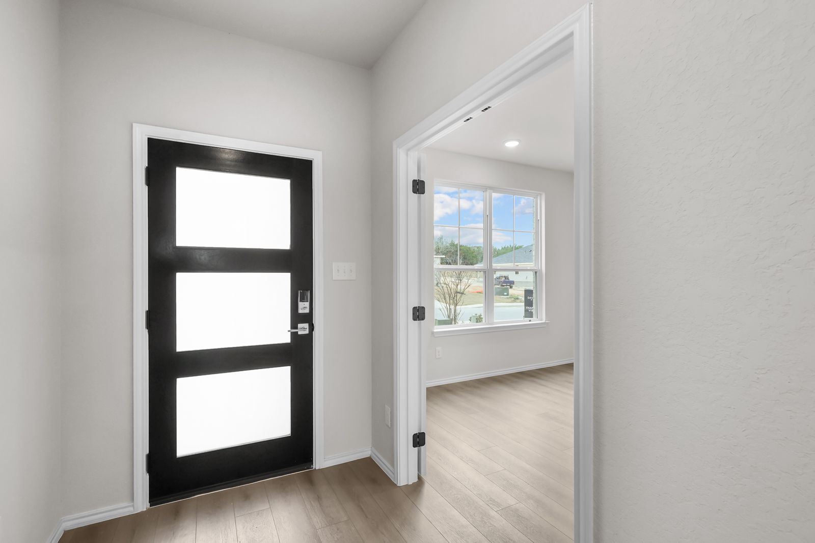 Modern black front door entry in The Sycamore B floor plan with light wood flooring and adjacent flex room.