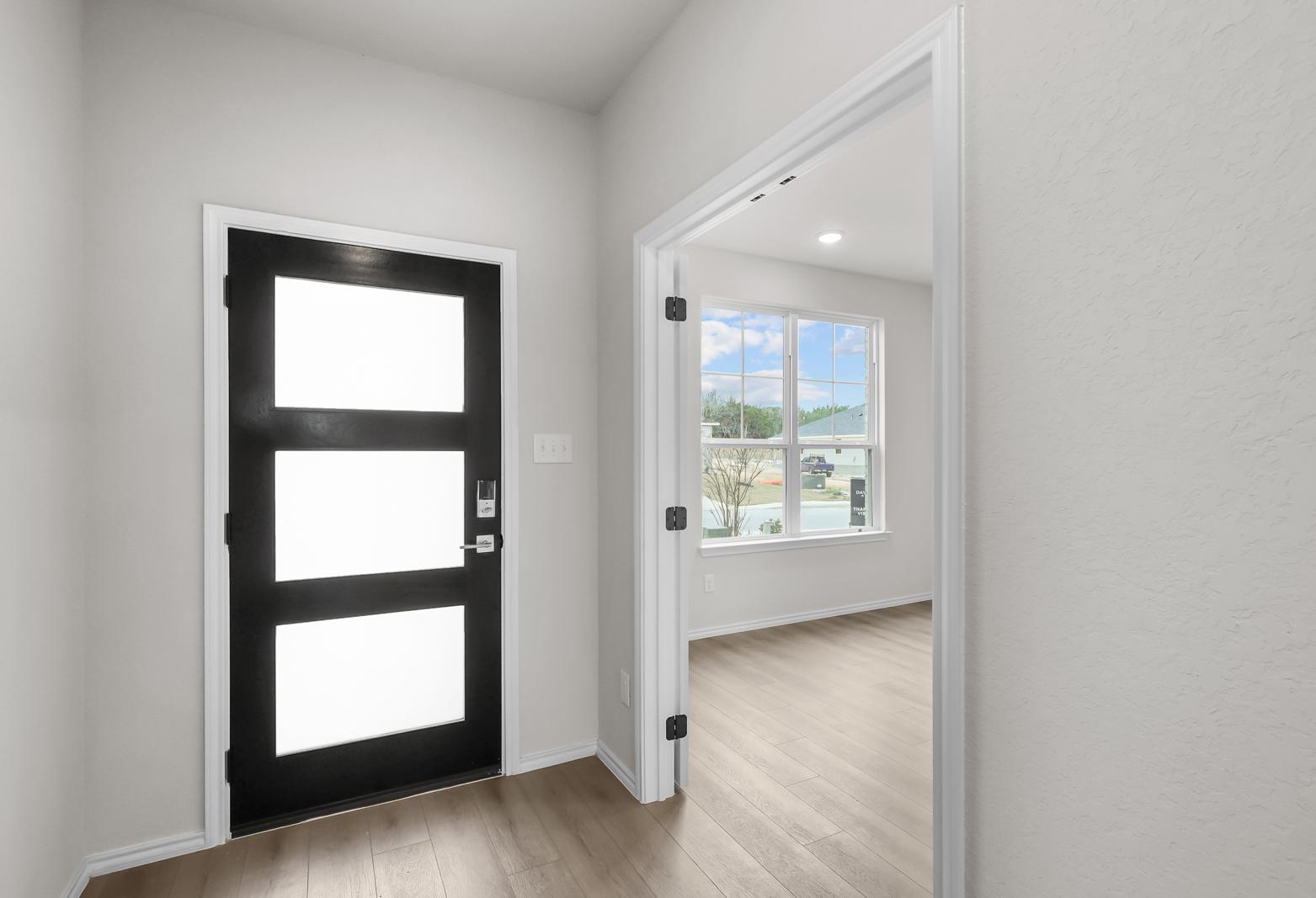 Modern black front door entry in The Sycamore B floor plan with light wood flooring and adjacent flex room.