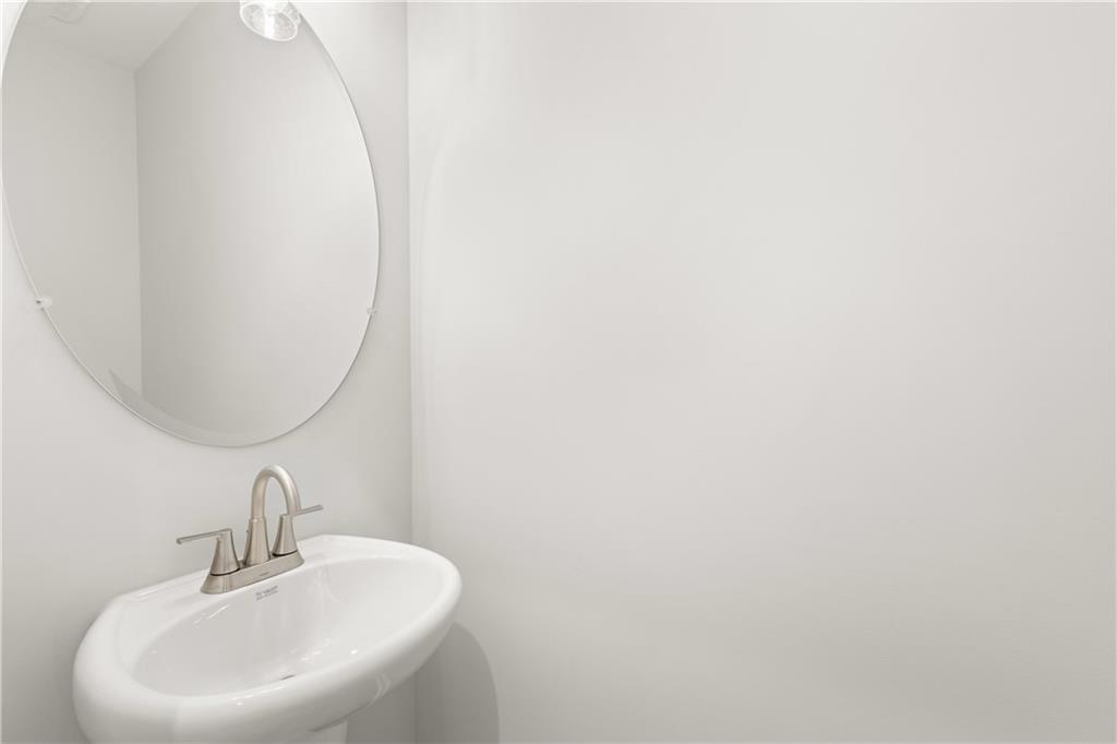 Modern powder room with white pedestal sink, round mirror, and brushed nickel faucet in The Cary A, Winder, Georgia