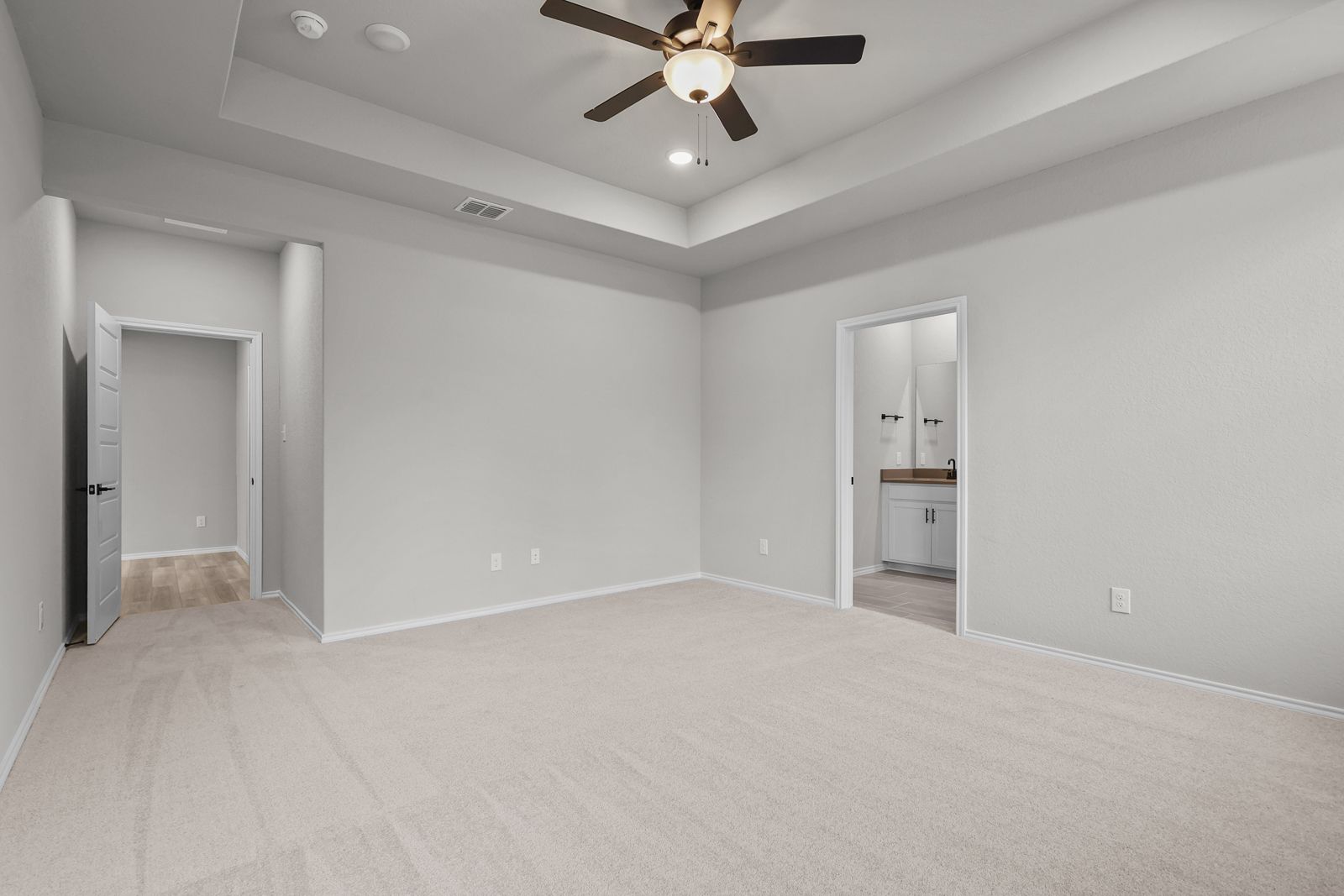 Spacious master suite in The Glenwood E featuring a tray ceiling, plush carpeting, and an attached private bathroom.