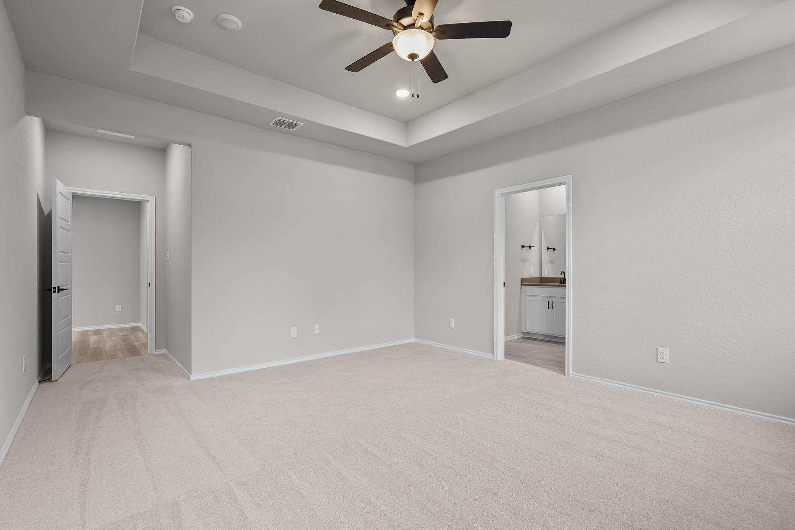 Spacious master suite in The Glenwood E featuring a tray ceiling, plush carpeting, and an attached private bathroom.