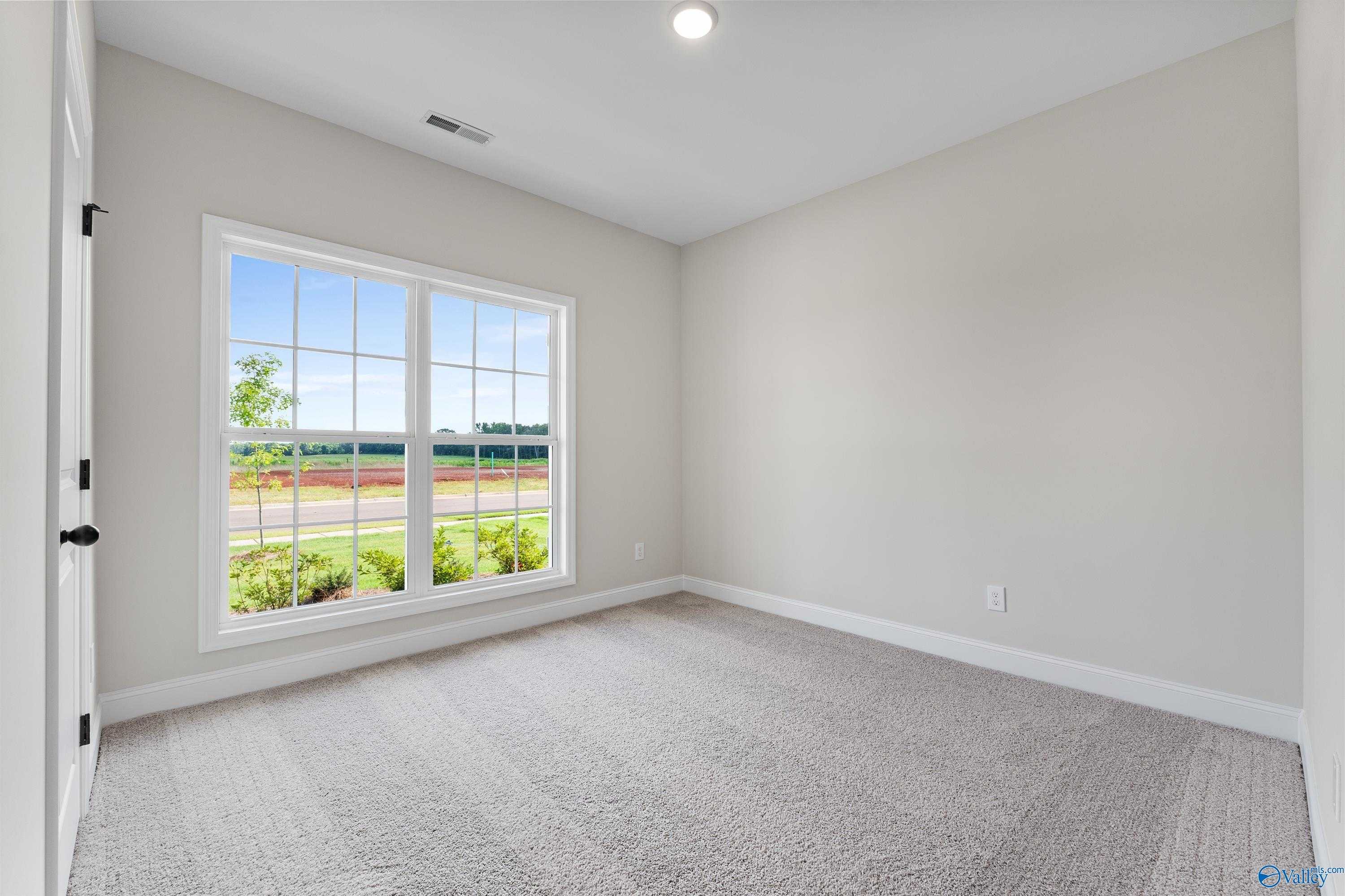 Bright empty bedroom with large window overlooking green yard in Davidson Homes The Franklin B, Hazel Green, Alabama