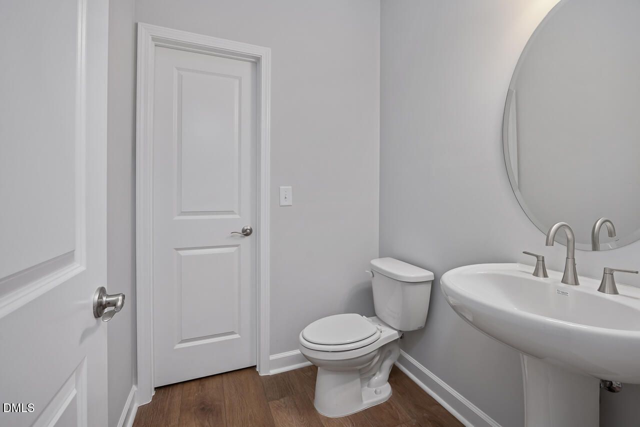 Modern half bathroom with pedestal sink, round mirror, and wood flooring in The Ashport L at Sage on North Main, Wake Forest.