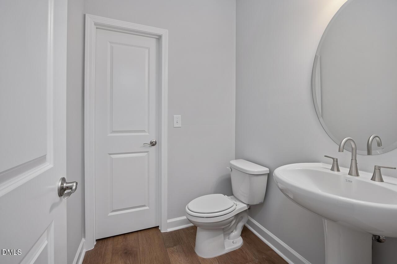 Modern half bathroom with pedestal sink, round mirror, and wood flooring in The Ashport L at Sage on North Main, Wake Forest.