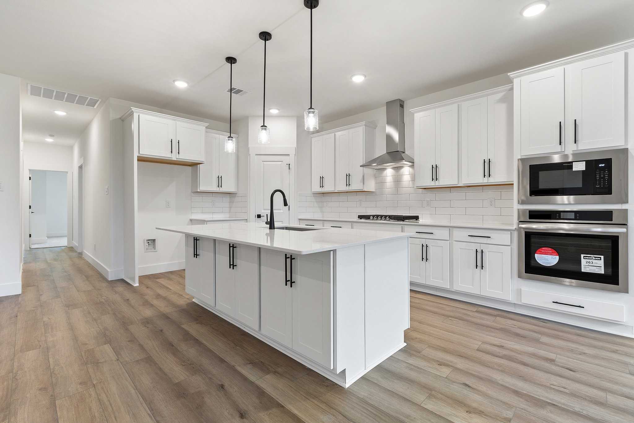 Modern white kitchen with large island, stainless double oven, subway tile backsplash in Davidson Homes Rockford C, Josephine TX
