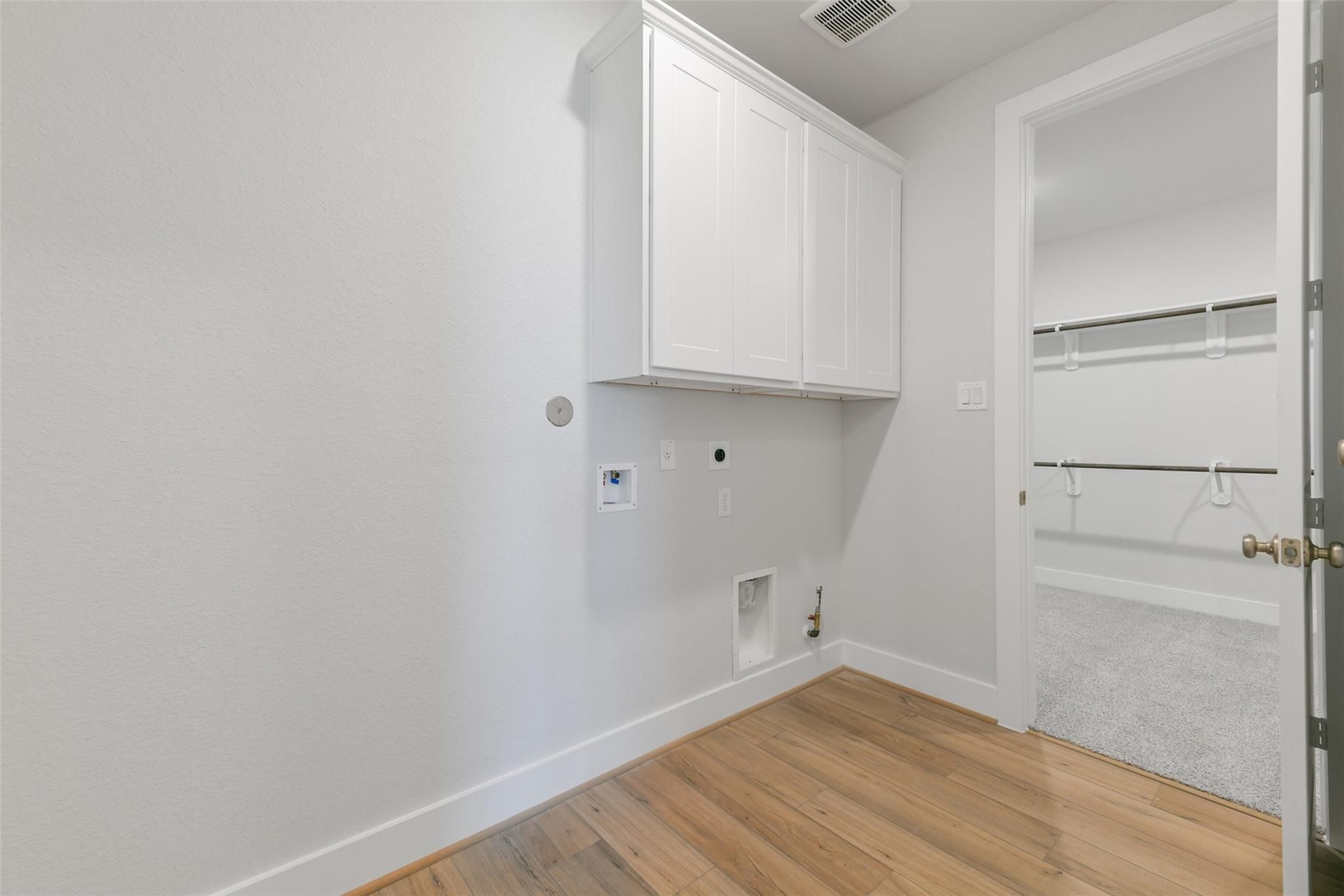 Modern laundry room with white cabinetry, open shelving, washer-dryer hookups, and hardwood floors in Davidson Homes The Edward A, Lago Mar
