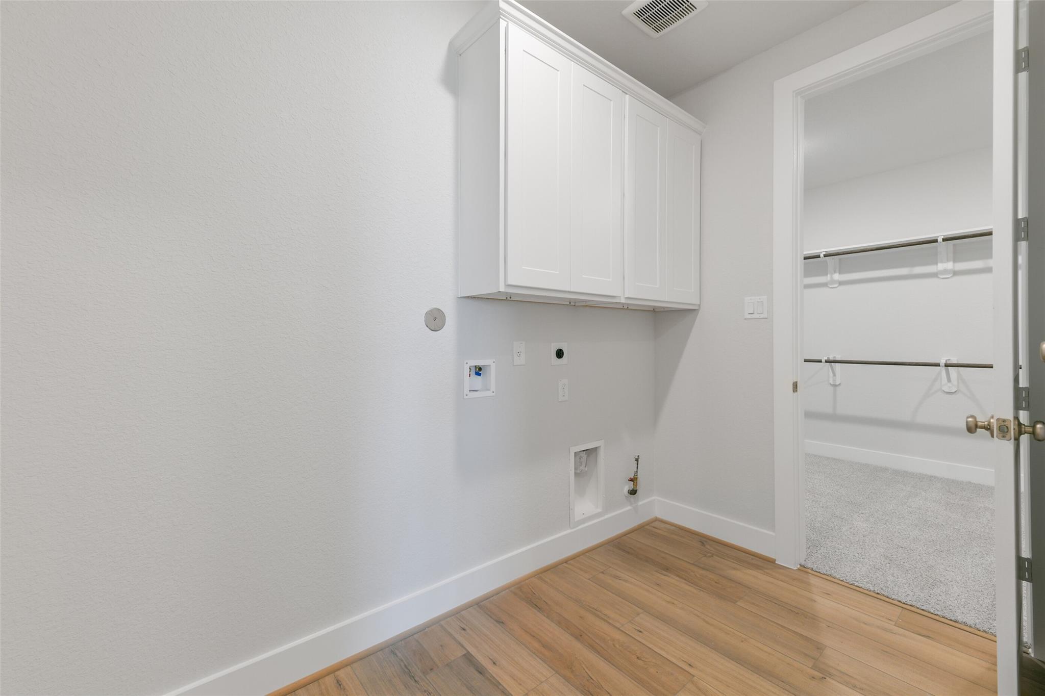 Modern laundry room with white cabinetry, open shelving, washer-dryer hookups, and hardwood floors in Davidson Homes The Edward A, Lago Mar