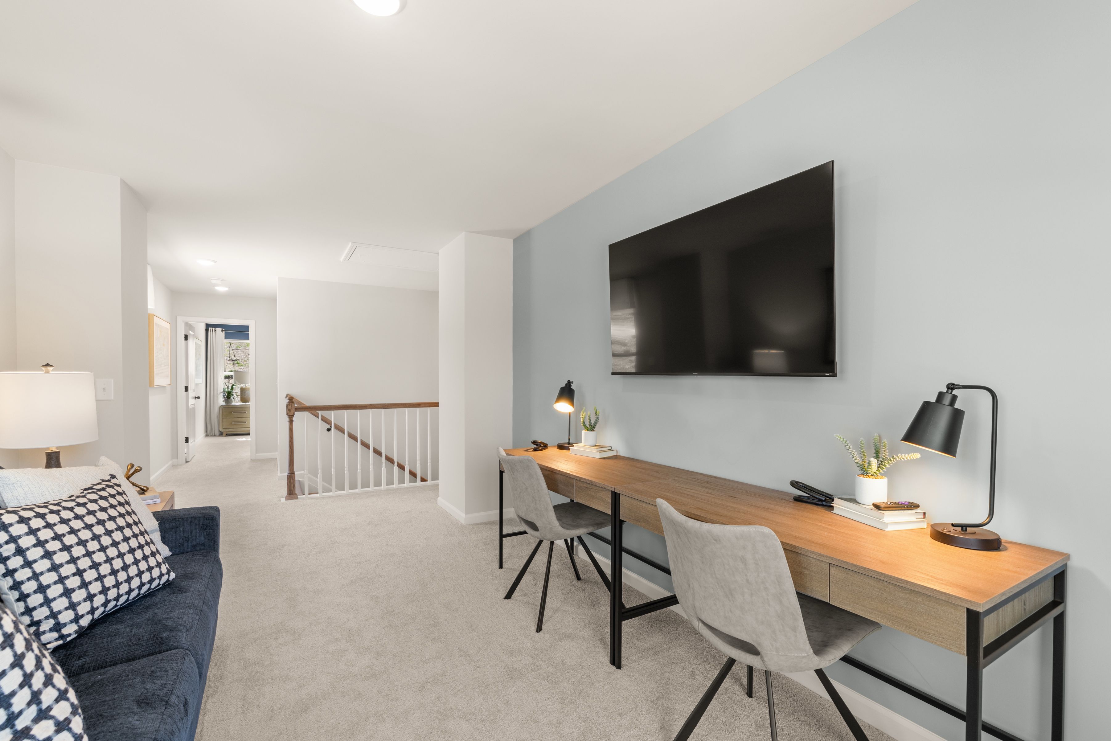 Spacious loft bonus room at The Bluffs in Canton GA featuring wooden desk, blue velvet sofa, wall TV, and modern lamps