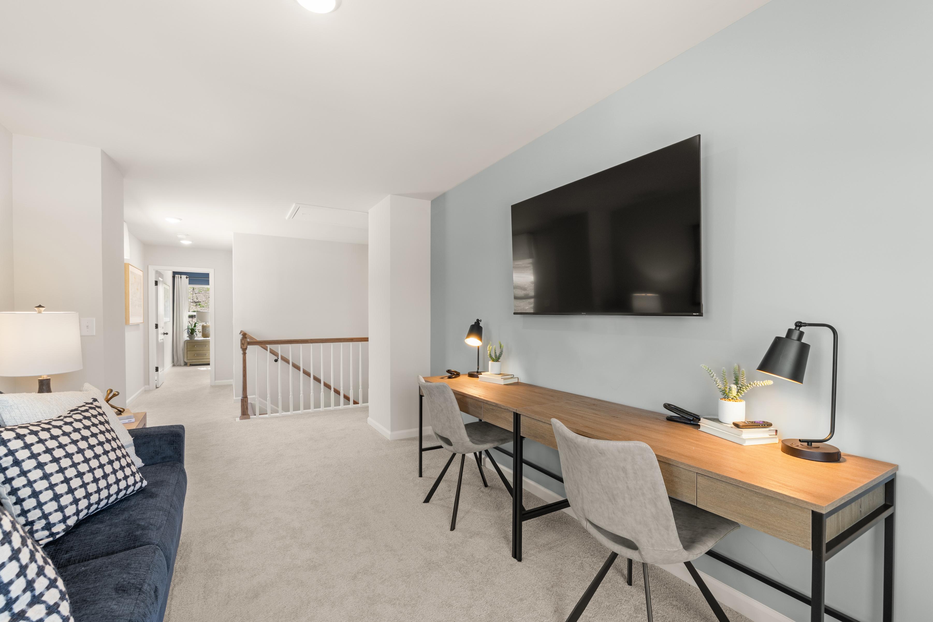 Spacious loft bonus room at The Bluffs in Canton GA featuring wooden desk, blue velvet sofa, wall TV, and modern lamps