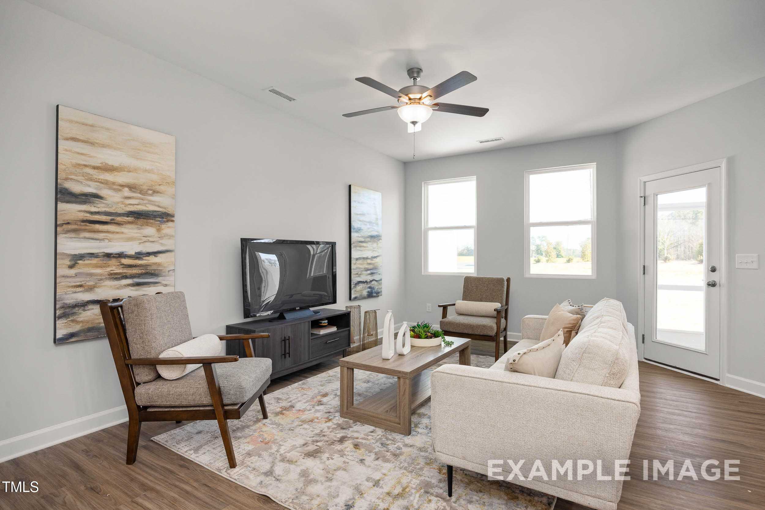 Cozy modern living room with beige sofa, armchairs, TV on media console, large windows, ceiling fan in Davidson Homes The Graham, Fuquay-Varina NC