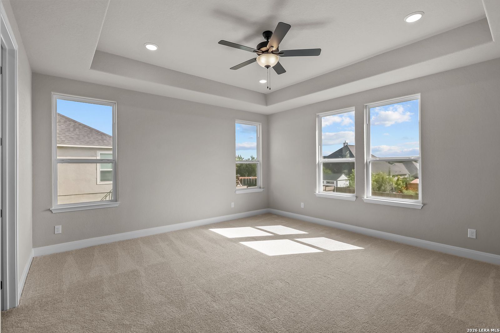 Bright bedroom with tray ceiling, ceiling fan, and multiple windows in Davidson Homes The Foster E, Castroville, Texas