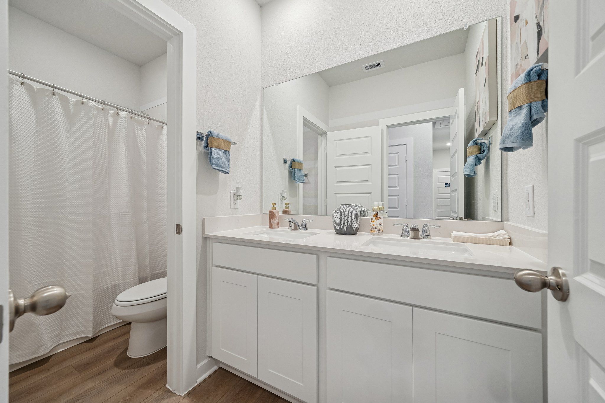 Modern bathroom at Spring Branch Crossing in Conroe TX with double vanity, white shower curtain, and hardwood floors