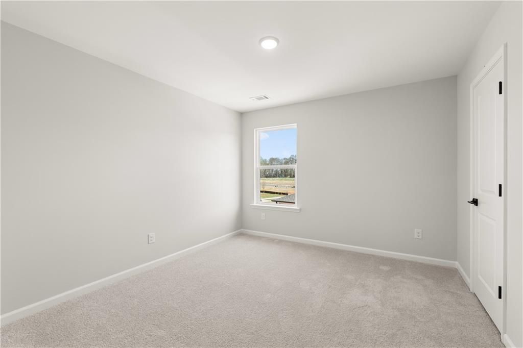 Bright bedroom with light gray walls, plush carpet, and window view in Davidson Homes The Hickory B, Winder, Georgia