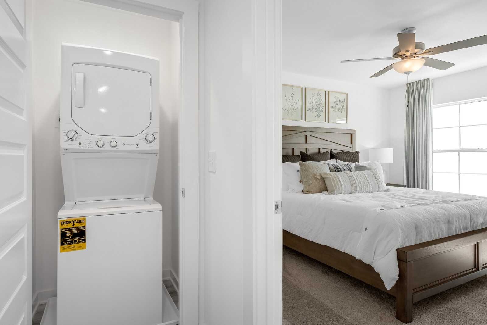 White stacked washer-dryer in laundry closet adjacent to cozy bedroom with ceiling fan in Davidson Homes The Cumberland B, Gallatin TN
