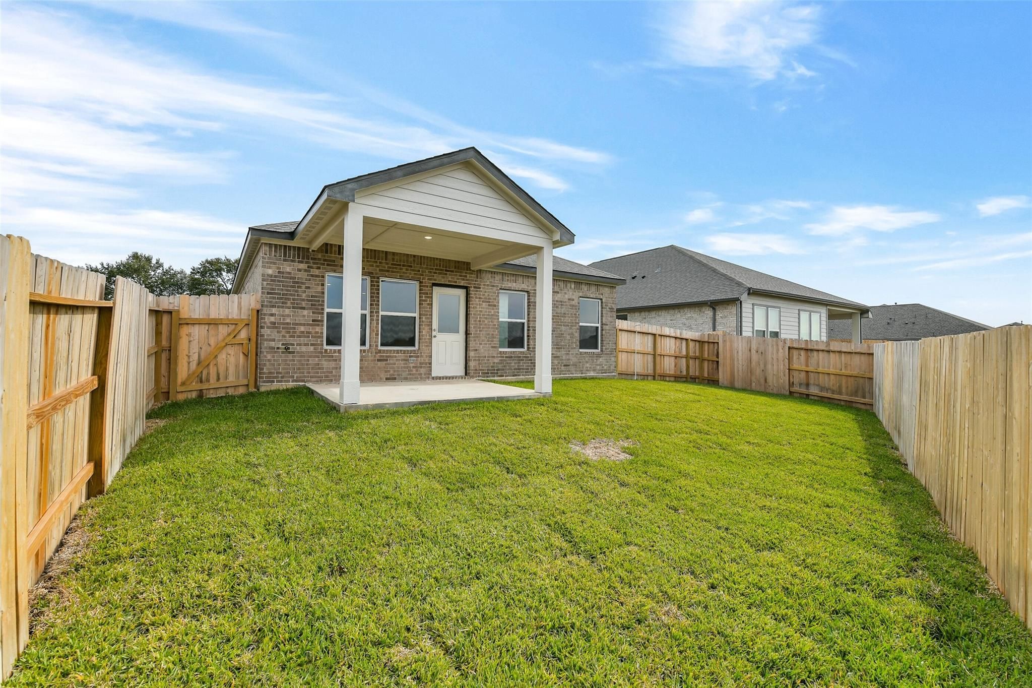 Modern 1-story brick home with 3-car garage, covered porch, and fenced grassy backyard in Windmill Estates, Magnolia, Texas