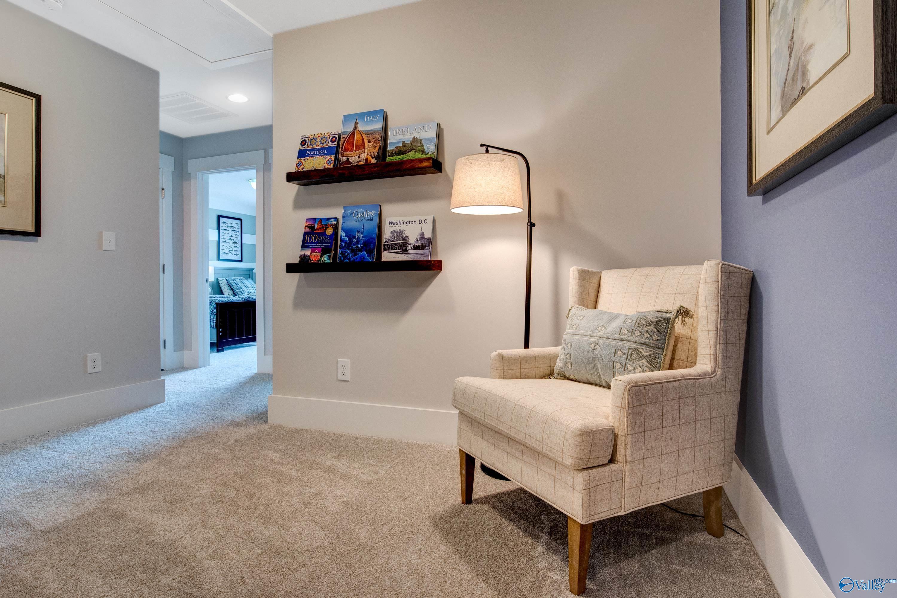 Cozy beige armchair with pillow, arched floor lamp, and floating bookshelves in light blue hallway of Davidson Homes The Covington C, Decatur, Alabama