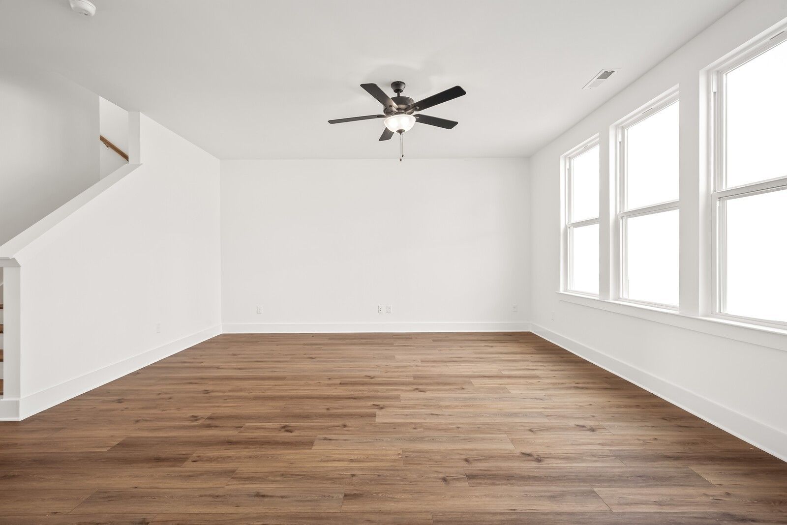 Bright spacious living room with hardwood floors, large sunny windows, ceiling fan, and open staircase in The Logan C home, Gallatin, TN