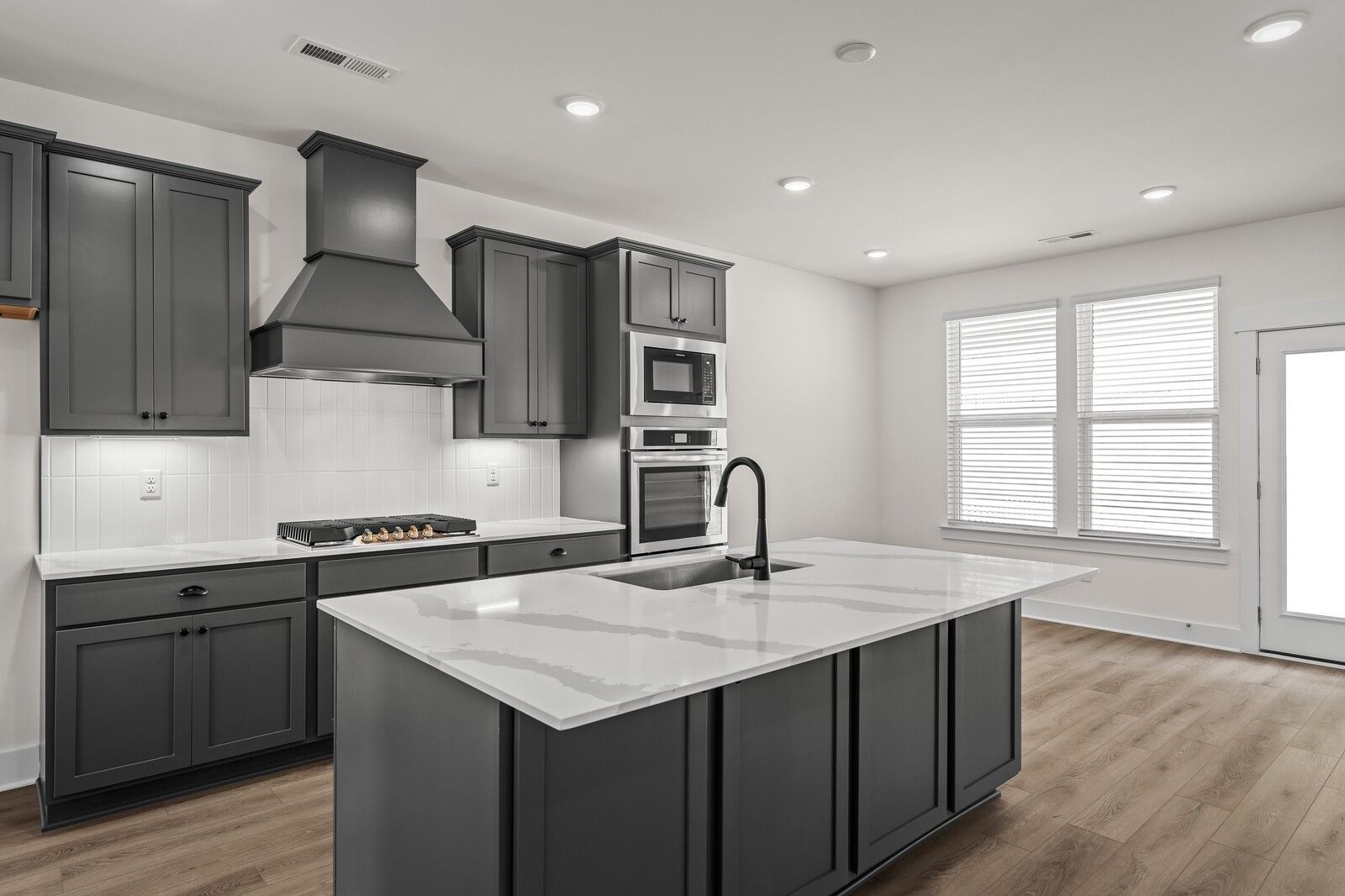 Modern kitchen with dark gray cabinets, quartz island, and stainless appliances in The Willow at Woods Crossing, Gallatin.