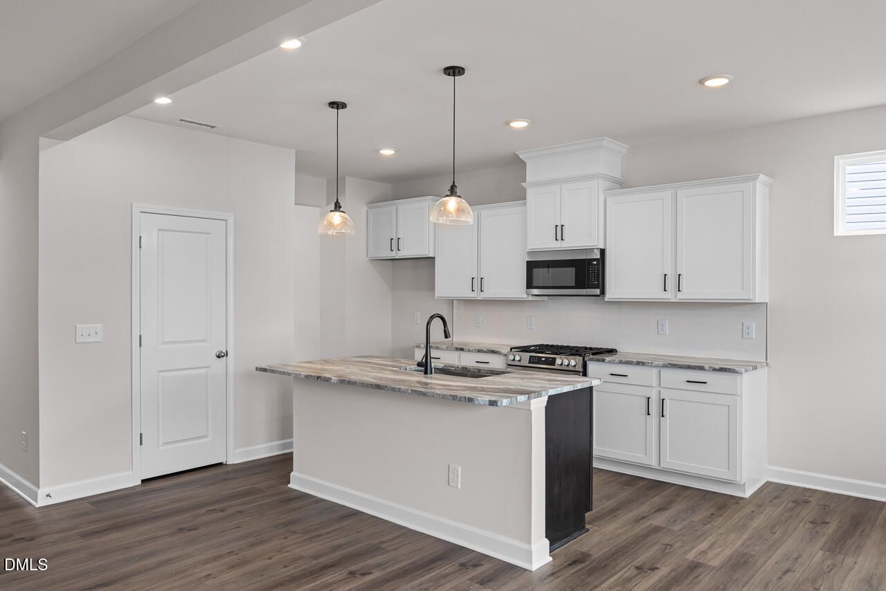 Modern kitchen with white cabinets, stone island, and pendant lighting in The Willow B floor plan, Woodland Crossing.