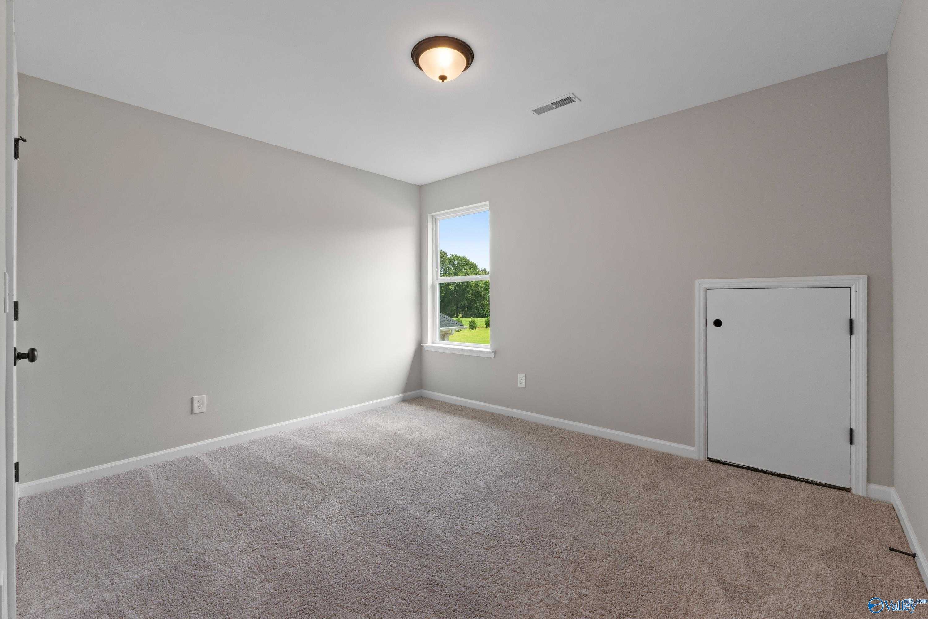 Bright secondary bedroom with large window overlooking green field, beige walls, and carpet in Davidson Homes The Dorado, Huntsville AL