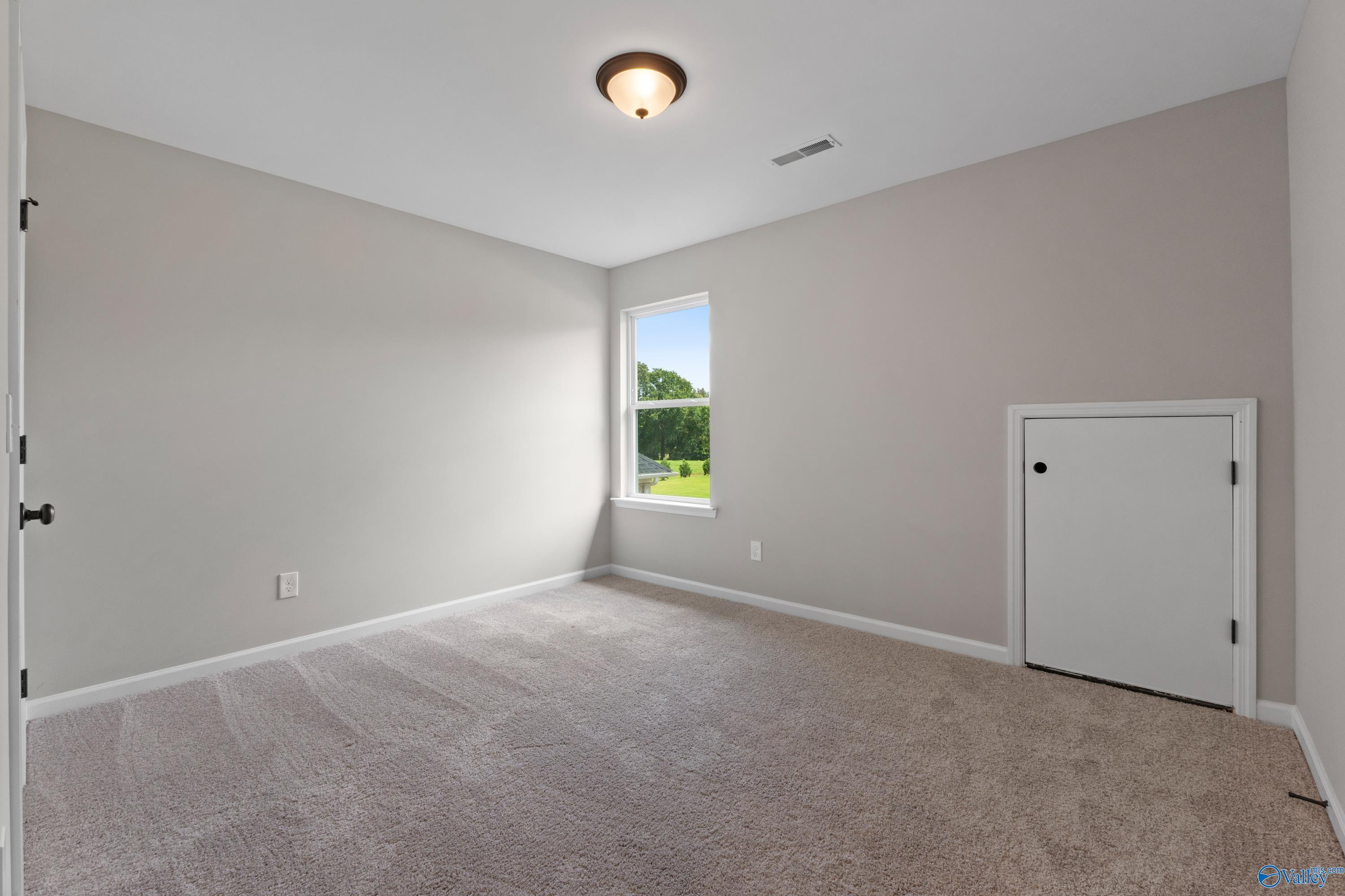 Bright secondary bedroom with large window overlooking green field, beige walls, and carpet in Davidson Homes The Dorado, Huntsville AL