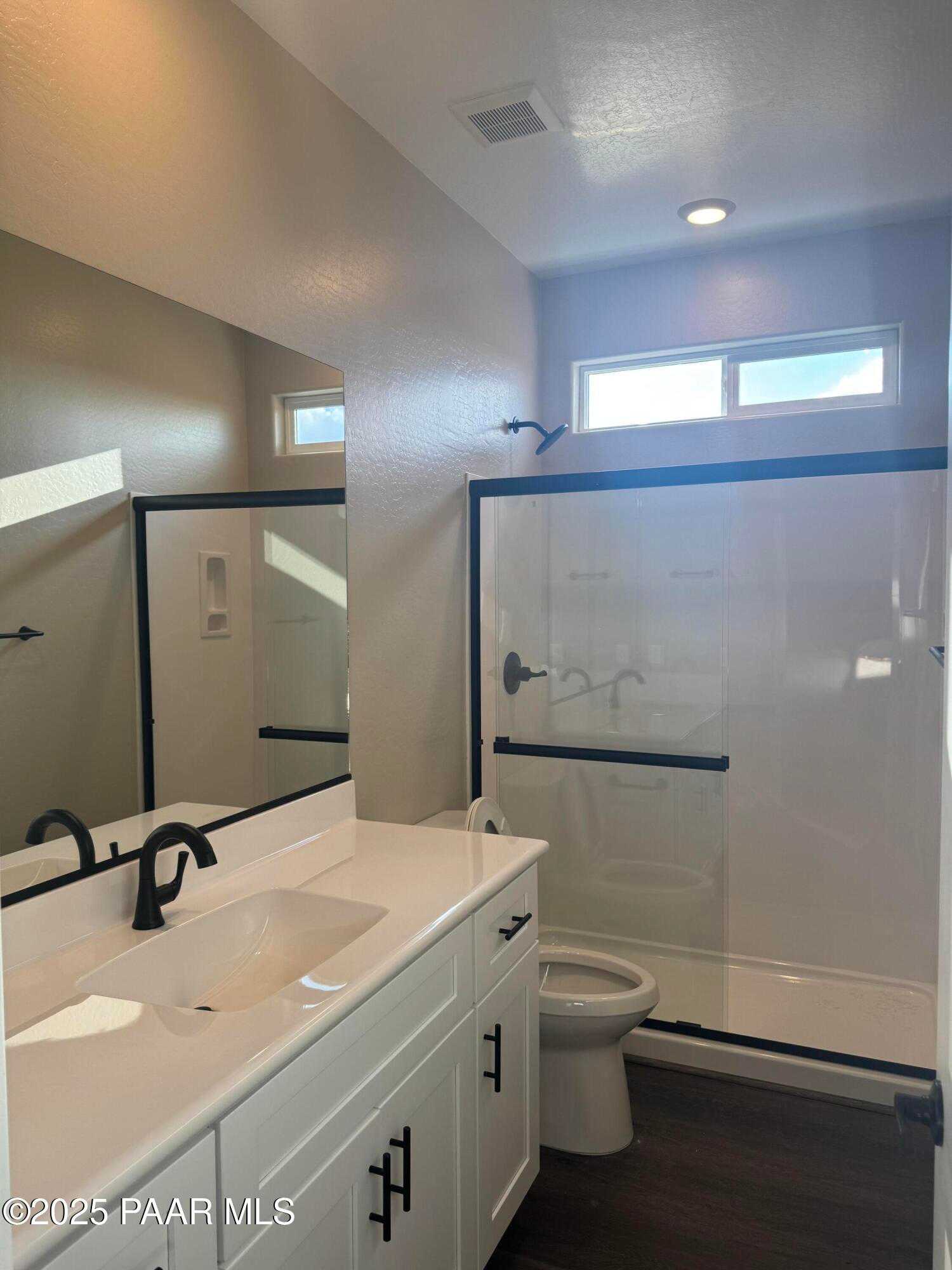 Spacious master bathroom with frameless glass shower, white vanity sink, and wood flooring in Evermore Homes The Sunrise A, Prescott Valley, AZ