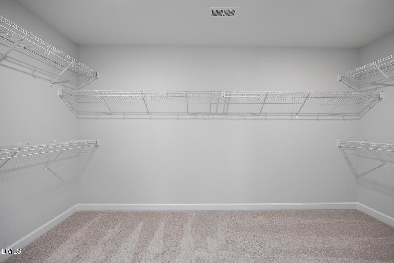 Spacious walk-in closet with white wire shelving and beige carpet in The Hickory II B by Davidson Homes, Zebulon, NC