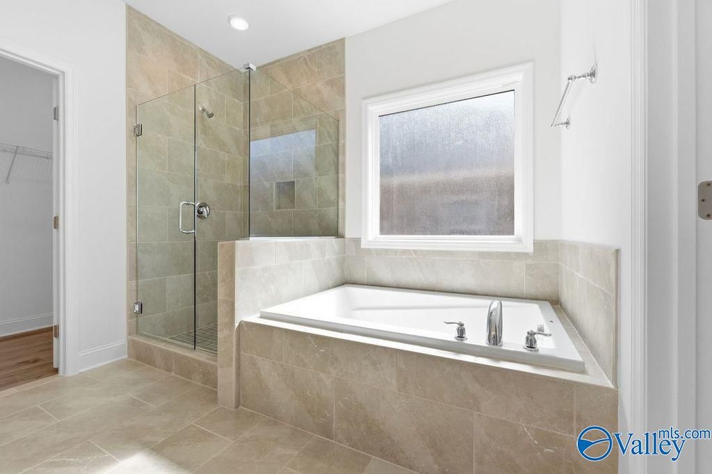 Modern master bathroom featuring glass shower, corner tub, and beige tile in Davidson Homes The Montgomery, Hartselle, AL