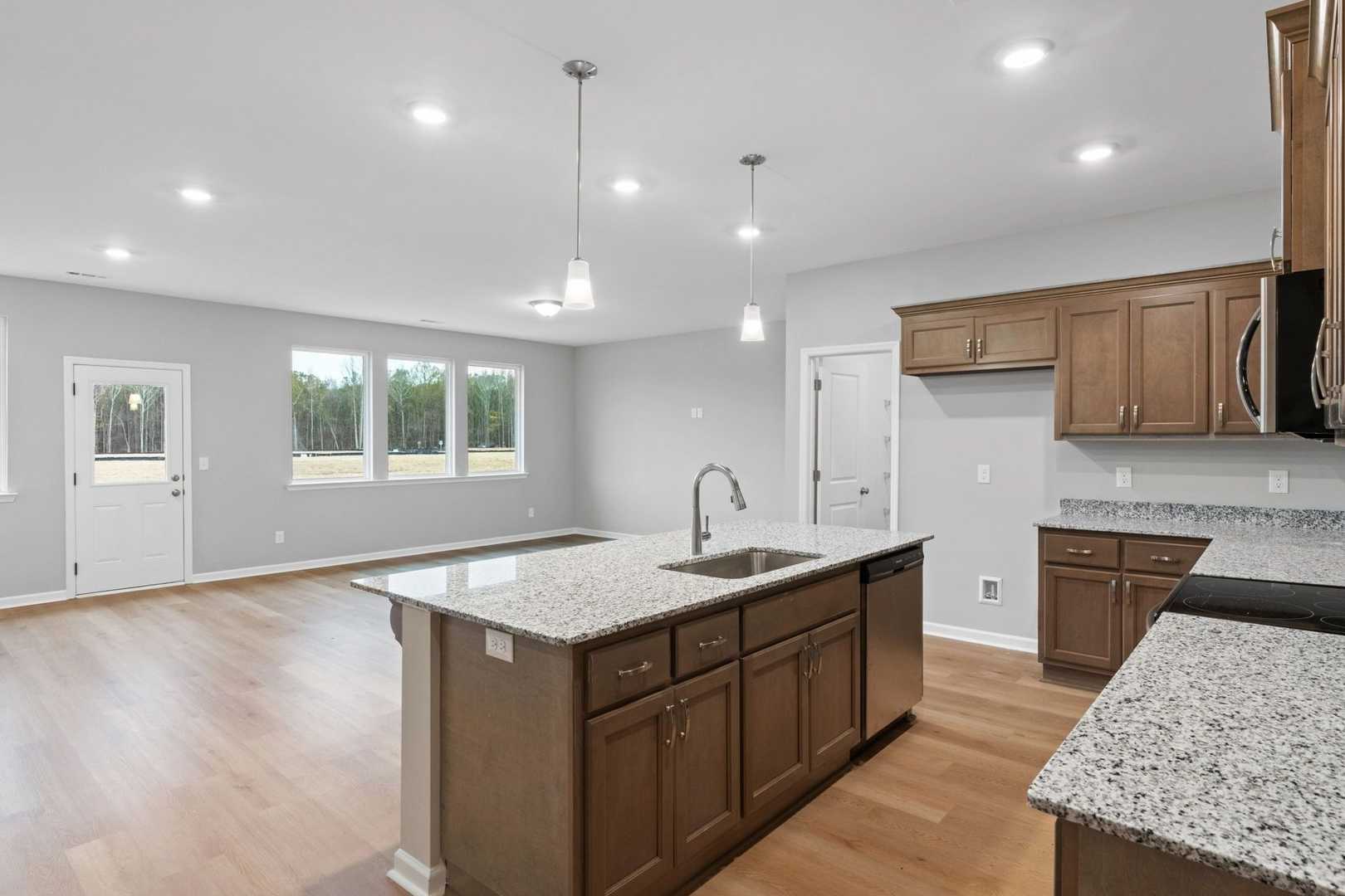 Modern kitchen in The Luna showcasing large granite island, shaker cabinets, open layout, and natural light