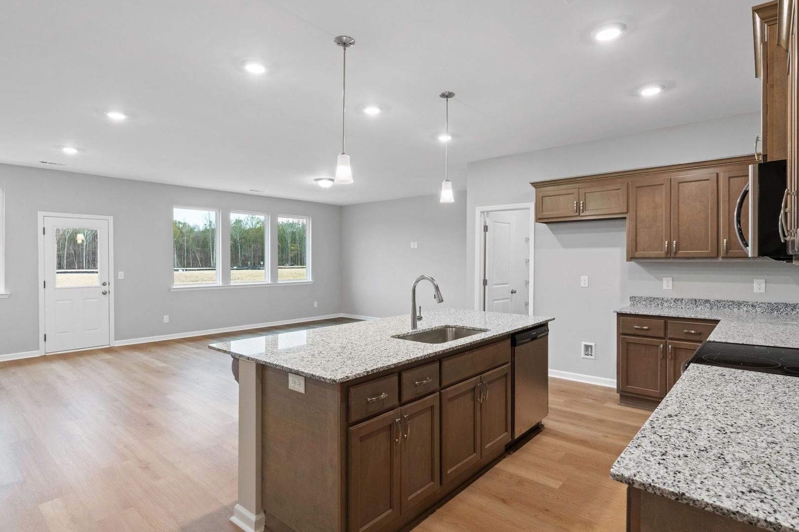 Modern kitchen in The Luna showcasing large granite island, shaker cabinets, open layout, and natural light