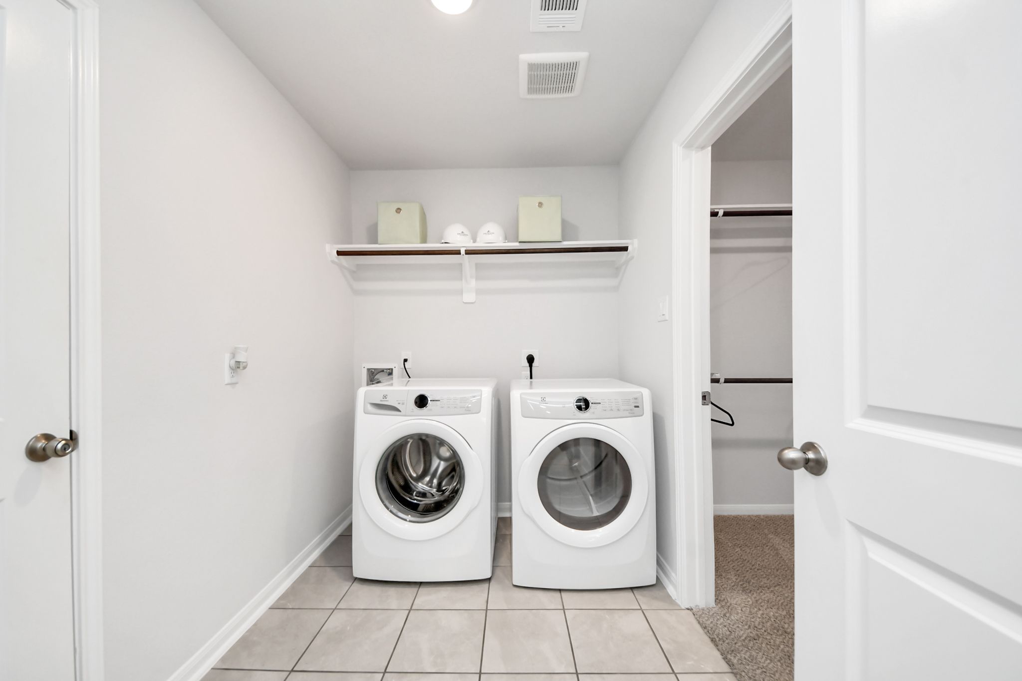 Laundry room with white appliances and storage shelving at Sunterra in Katy, Texas by Davidson Homes.