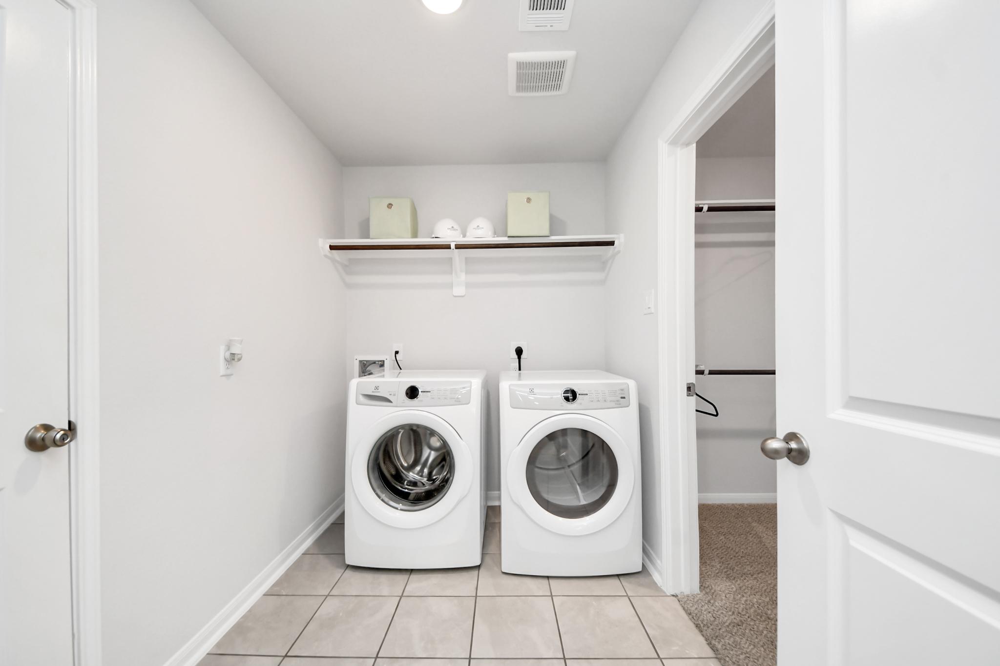 Laundry room with white appliances and storage shelving at Sunterra in Katy, Texas by Davidson Homes.