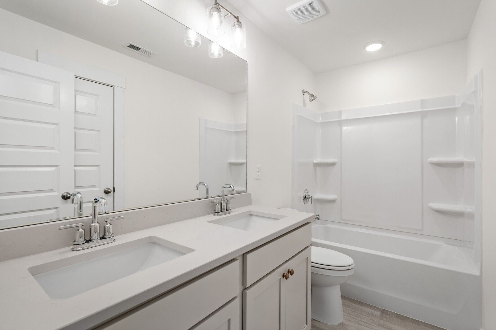 Modern bathroom with double quartz vanity, soaking tub, shower combo, and wood-look flooring in Davidson Homes The Ridgeport, Gallatin, TN