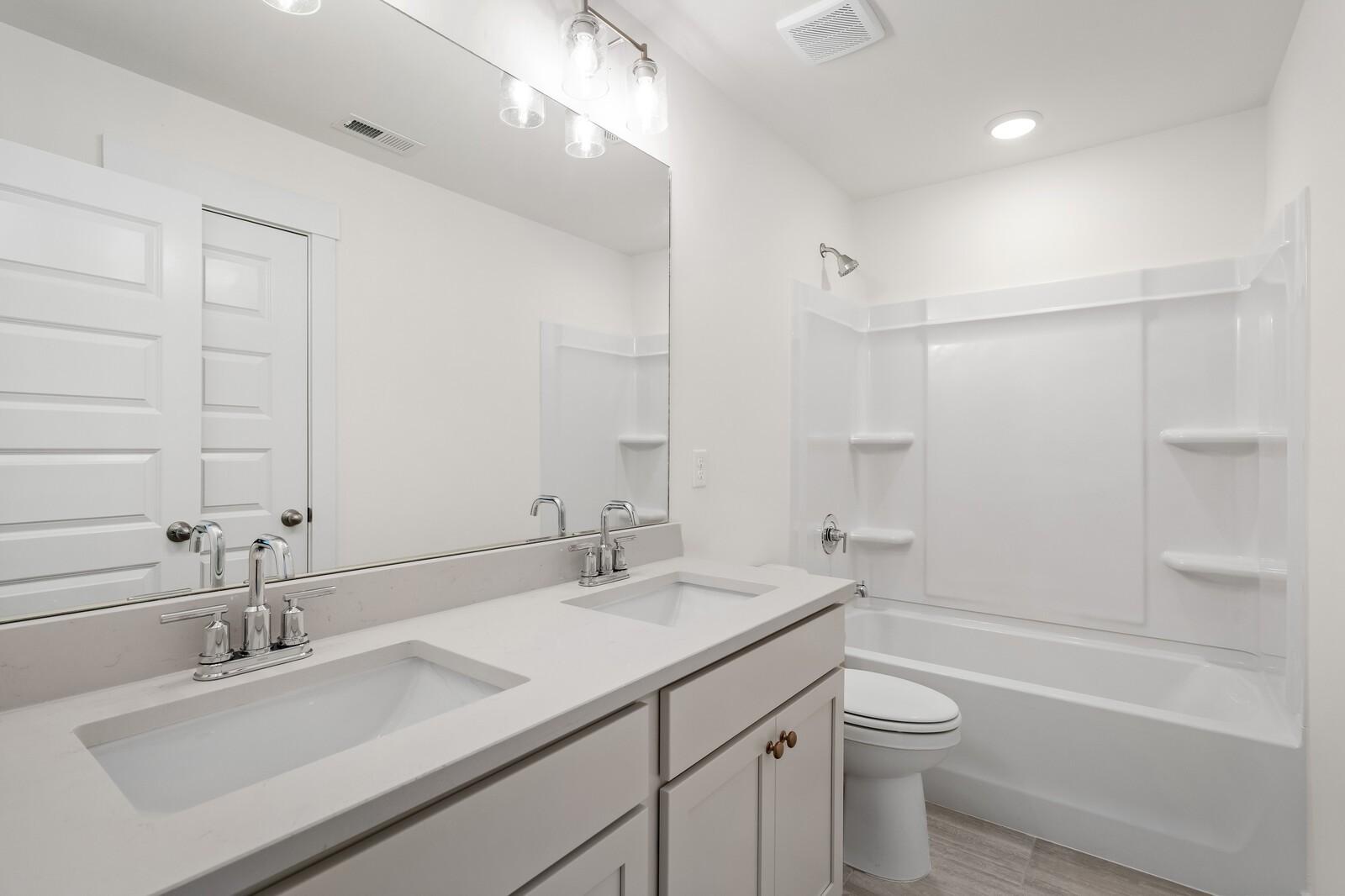 Modern bathroom with double quartz vanity, soaking tub, shower combo, and wood-look flooring in Davidson Homes The Ridgeport, Gallatin, TN