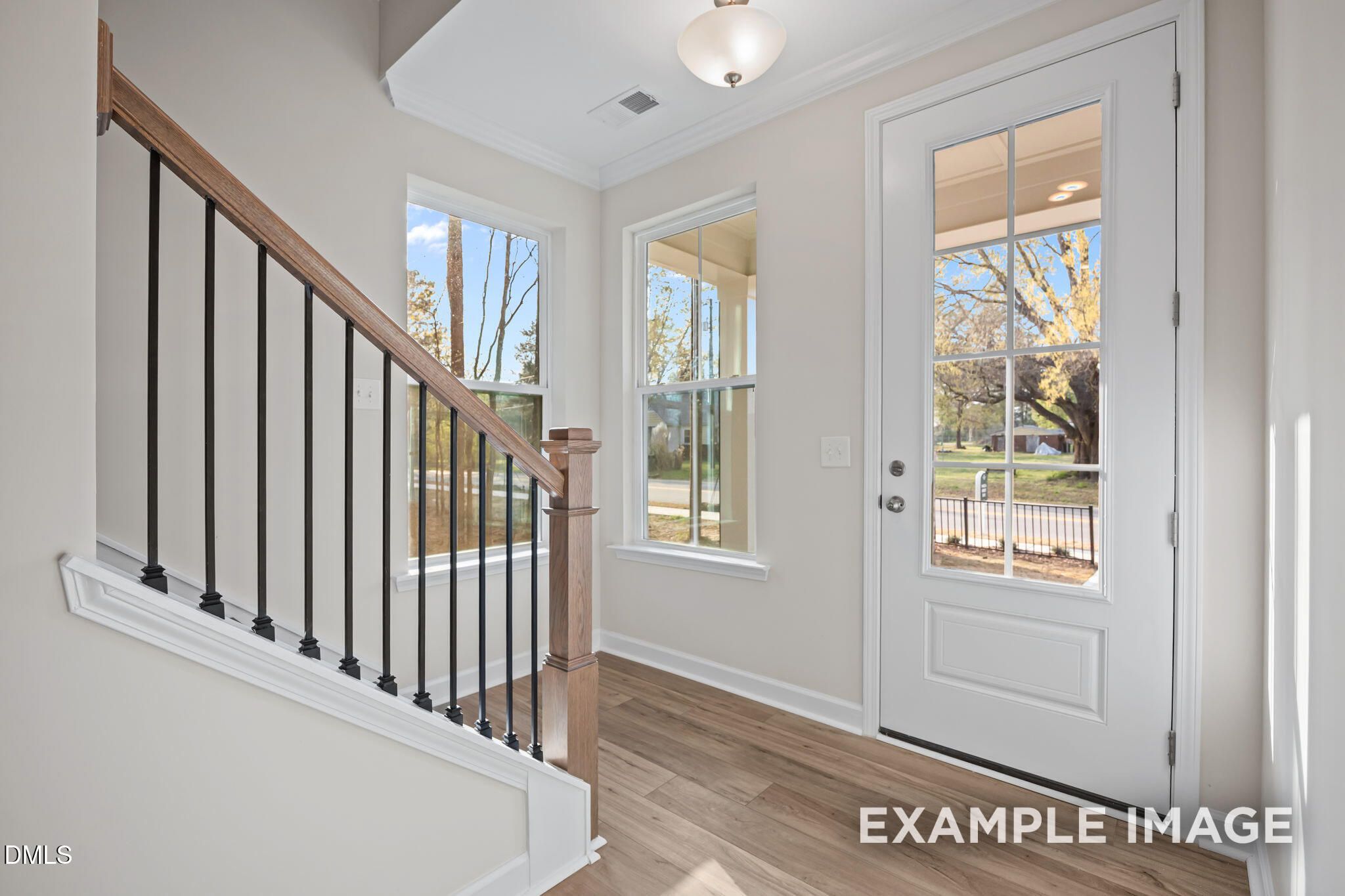 Bright entryway with wooden staircase, black iron balusters, and glass-paneled front door in Davidson Homes The Avery, Knightdale NC