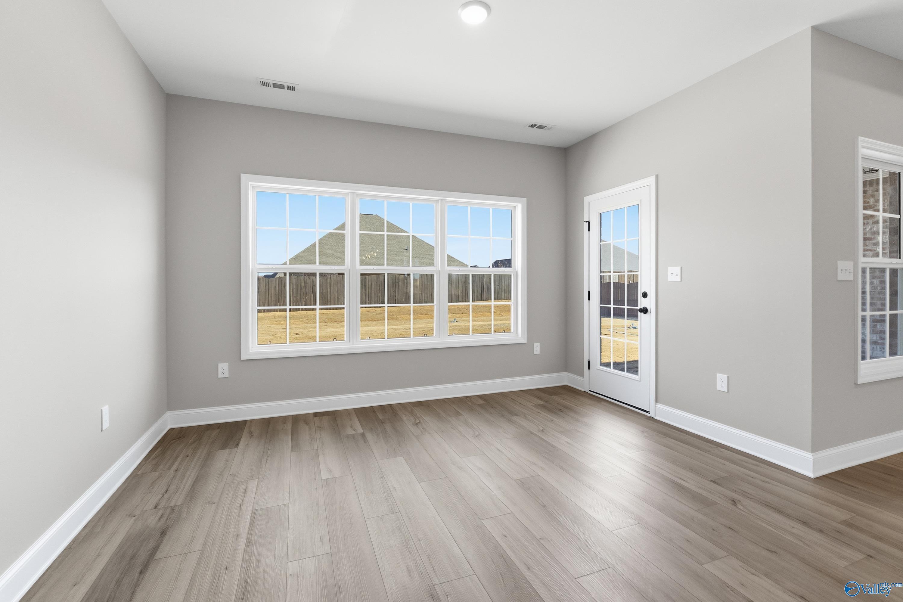 Bright family room with gray walls, hardwood floors, large windows, and glass door overlooking fields in Davidson Homes The Finleigh, Meridianville, Alabama