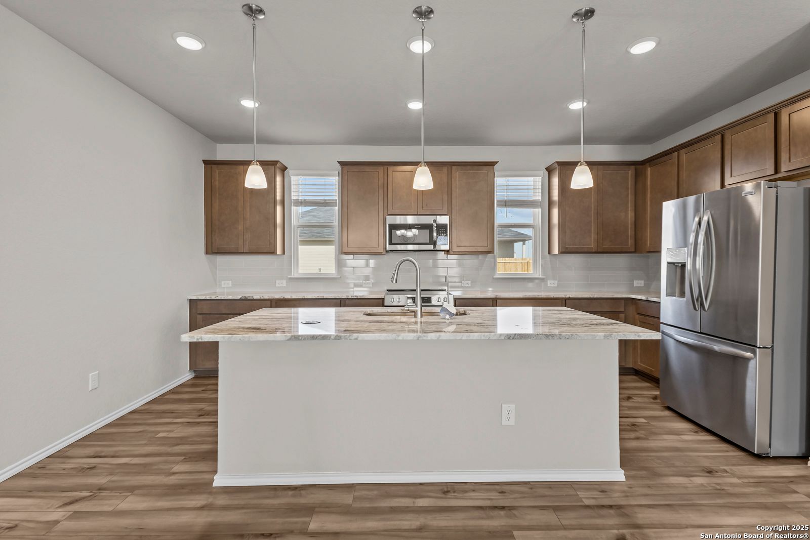 Modern kitchen with white island sink, stainless fridge, granite counters, and pendant lights in Davidson Homes The Collin B, Seguin TX