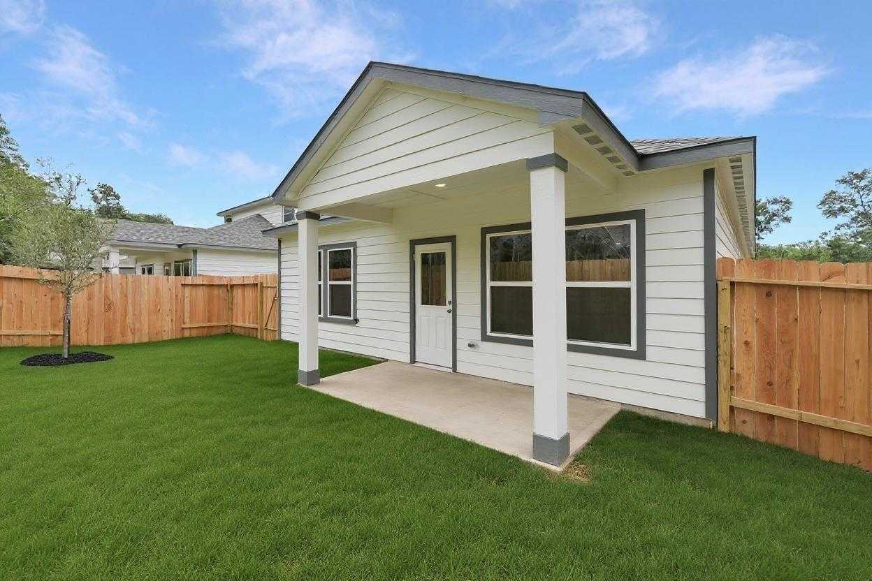 Modern white single-story home with covered front porch, columns, and green lawn in Caney Creek Place, Conroe, Texas