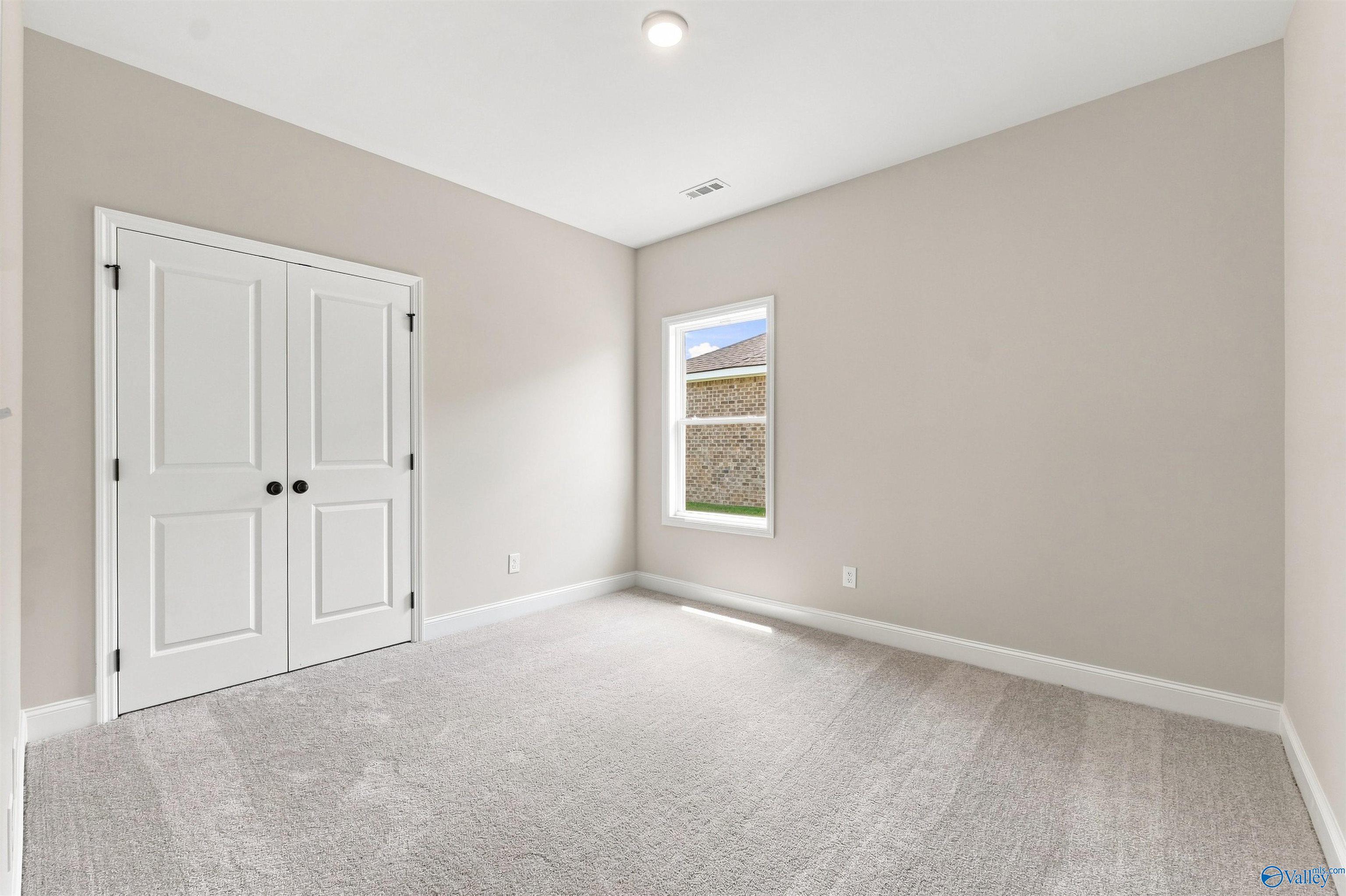 Bright bedroom with plush carpet, white double closet doors, and window in Davidson Homes The Everett B, Toney, Alabama