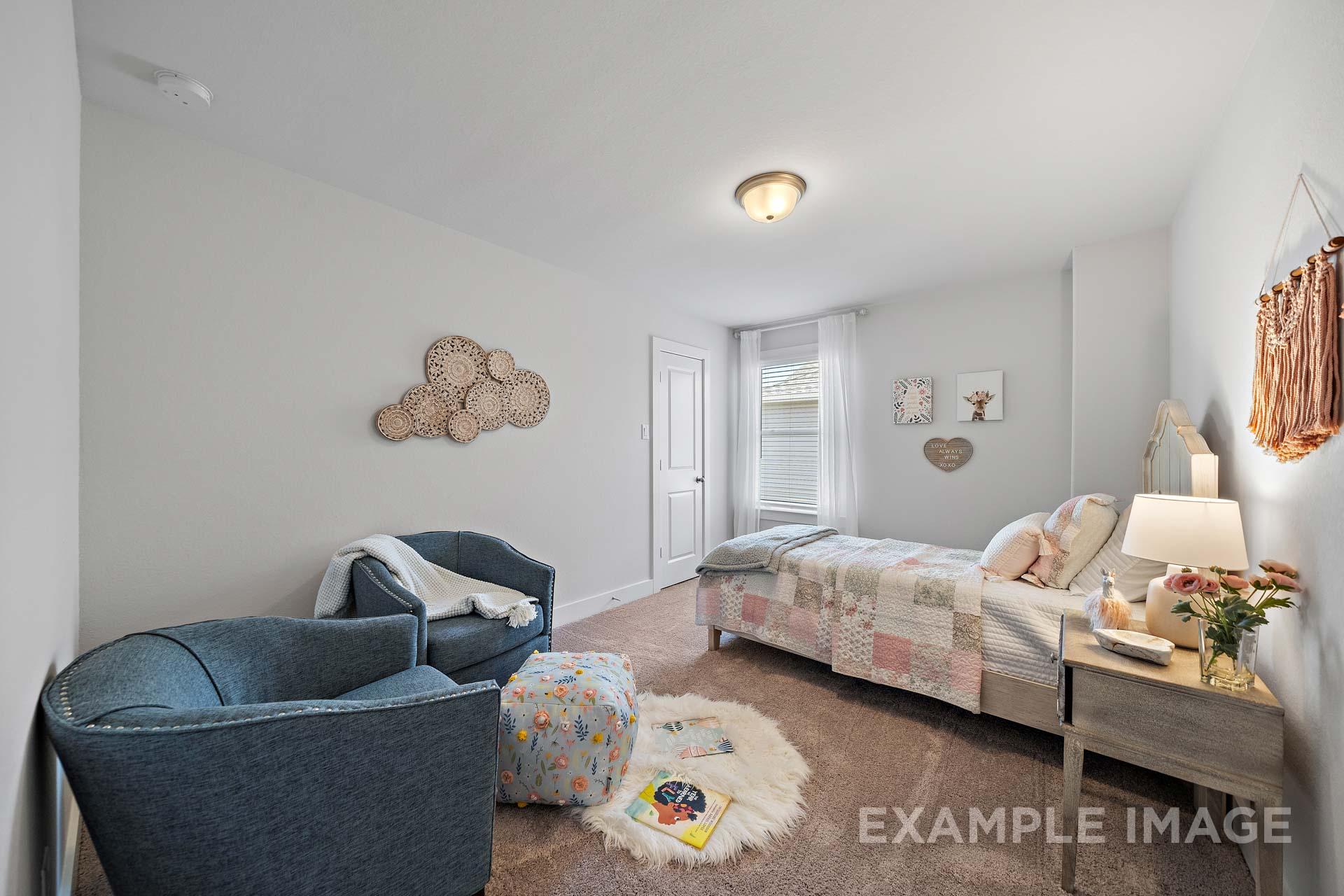 Cozy secondary bedroom in The Rose B by Davidson Homes featuring queen bed with quilt, blue armchairs, woven wall art, and fluffy rug